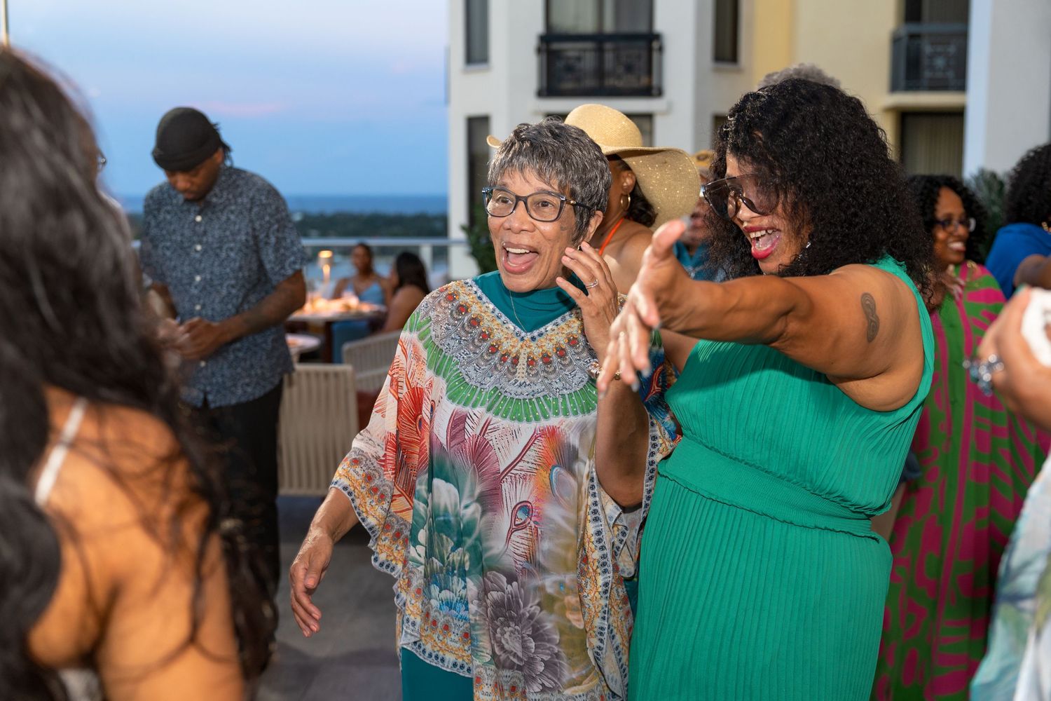 Party guests dancing and celebrating in an indoor venue with natural lighting.