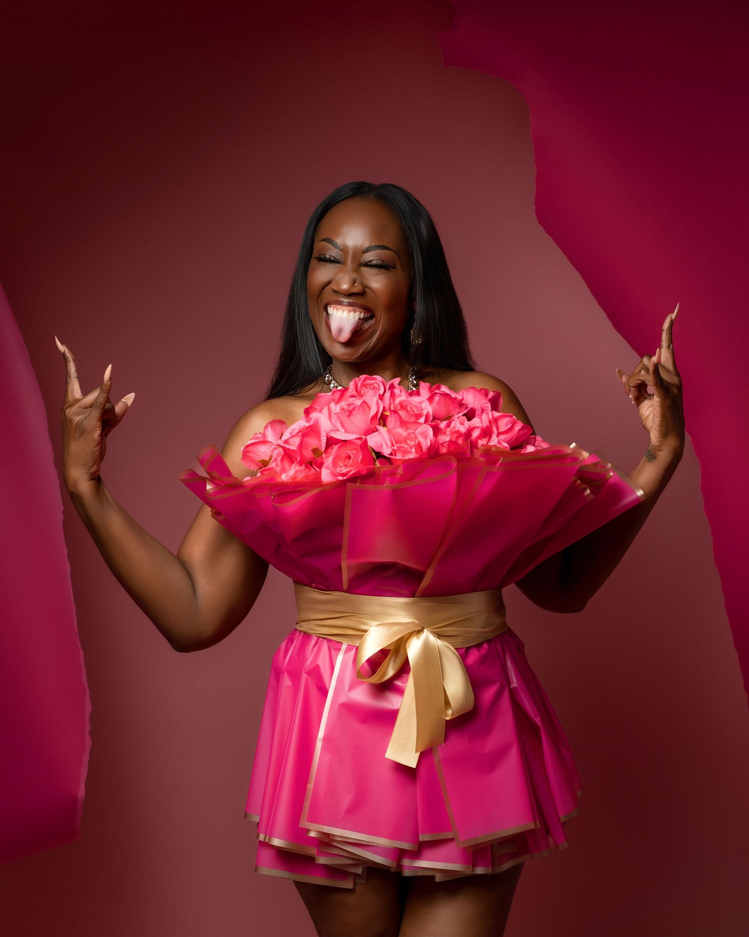Person in bright pink dress holding bouquet of pink flowers and making peace signs against magenta background.