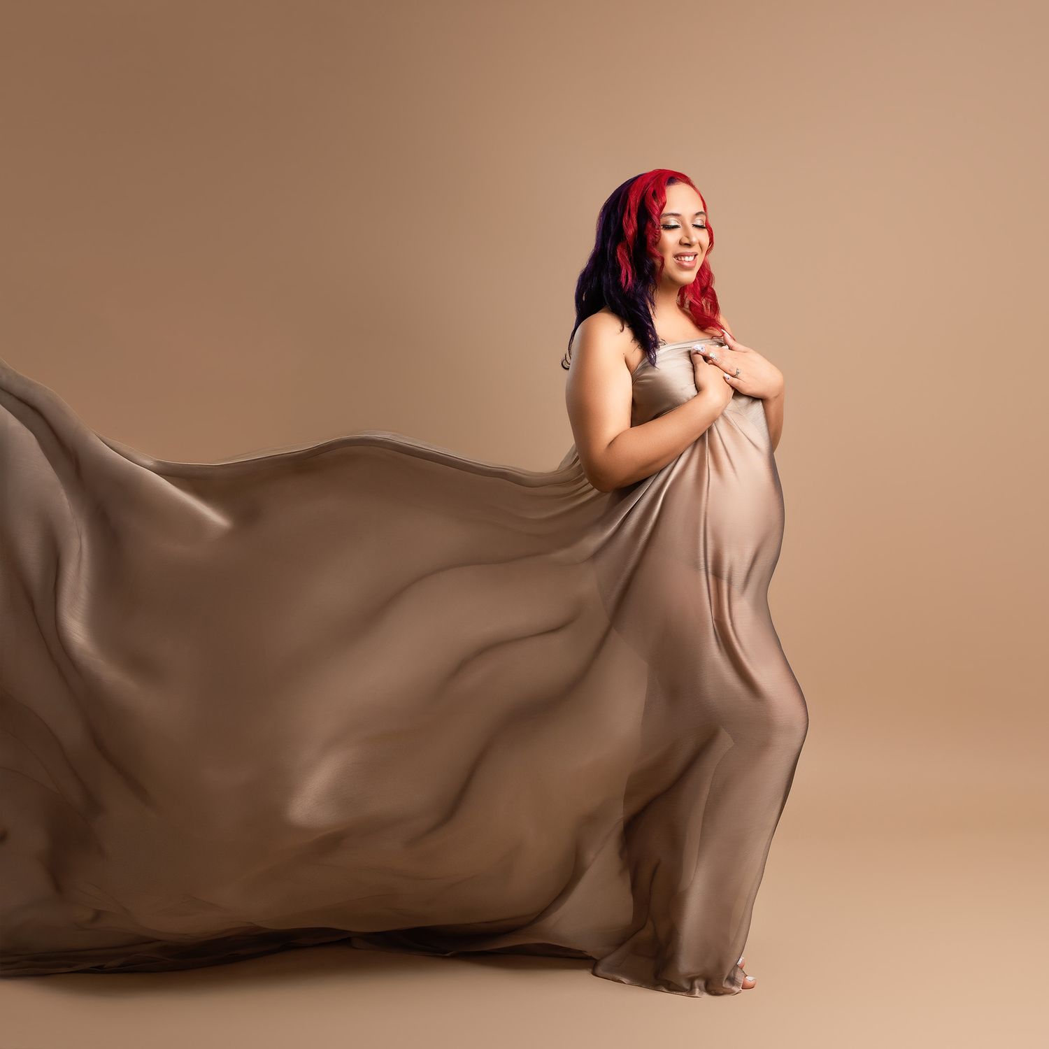 Maternity portrait with flowing taupe fabric against neutral background.