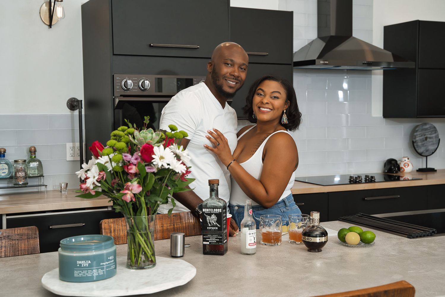 Happy couple embracing in modern kitchen with flowers and cocktail ingredients on counter.