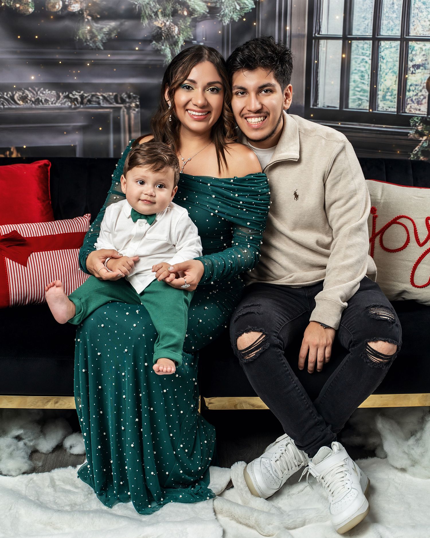 Intimate family portrait with parents and baby in coordinated holiday outfits against winter backdrop.