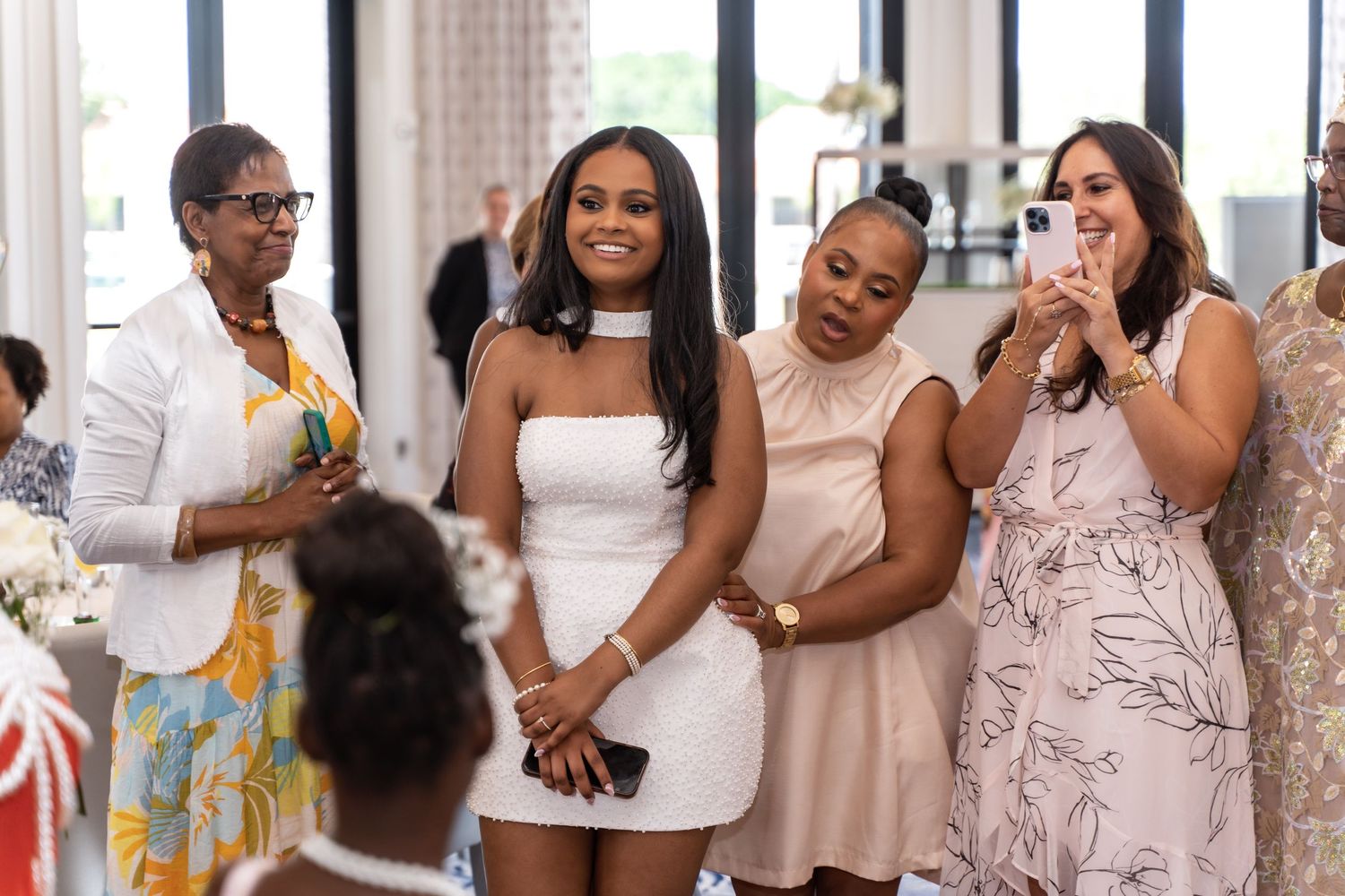 A group sharing a joyful reaction at a celebration with one guest wearing a white strapless dress.