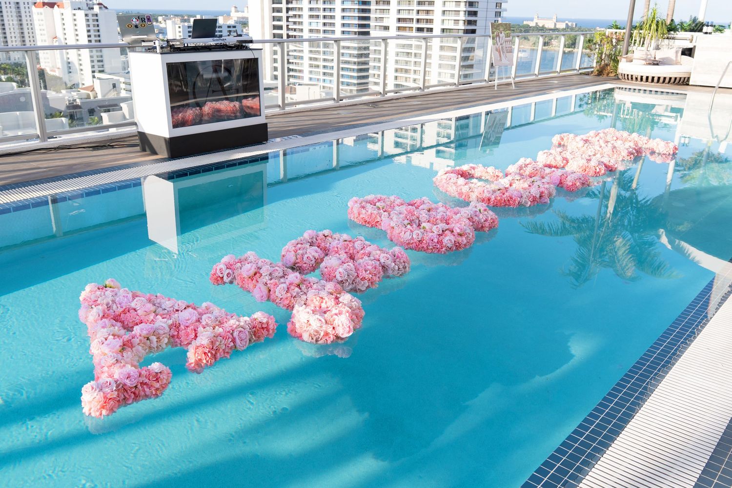 Pink floral decorations float in a rooftop infinity pool with urban cityscape views in the background.