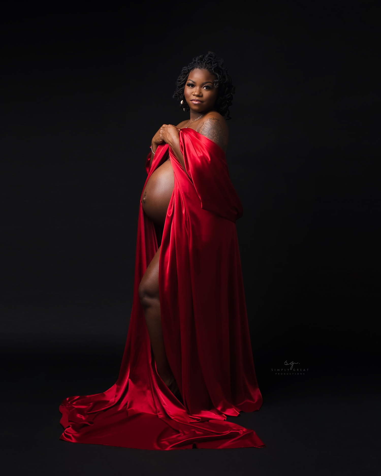 Dramatic maternity portrait with flowing red silk against dark background.