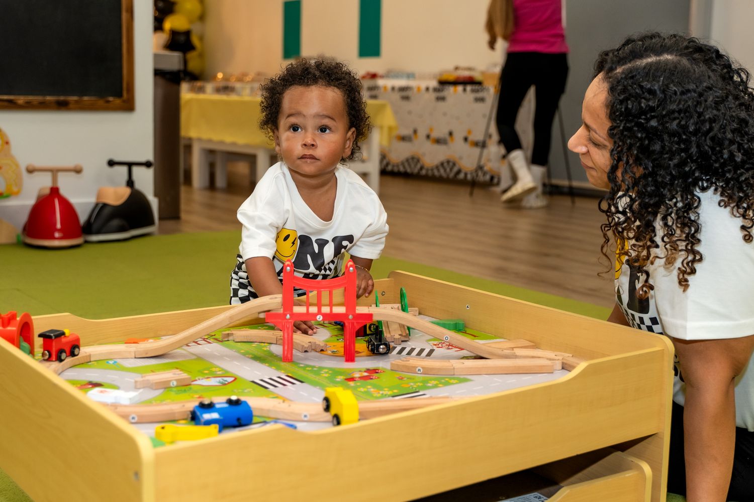 Toddler playing with toys at a wooden activity table while being supervised.