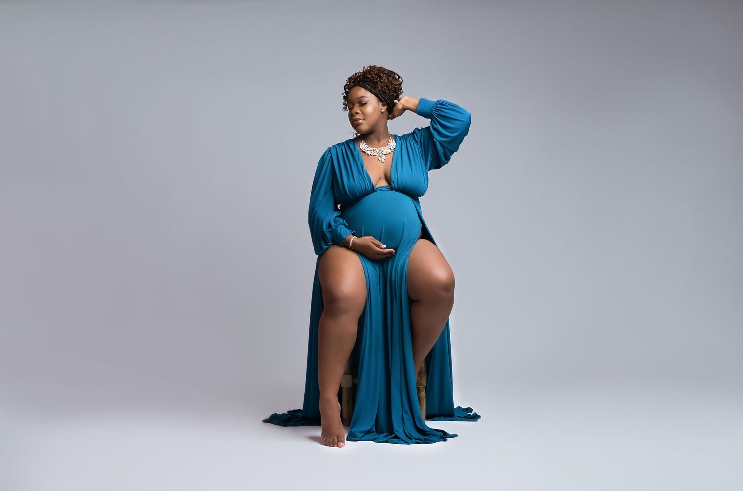 Maternity portrait showing a woman in a flowing blue dress posing gracefully against a gray background.