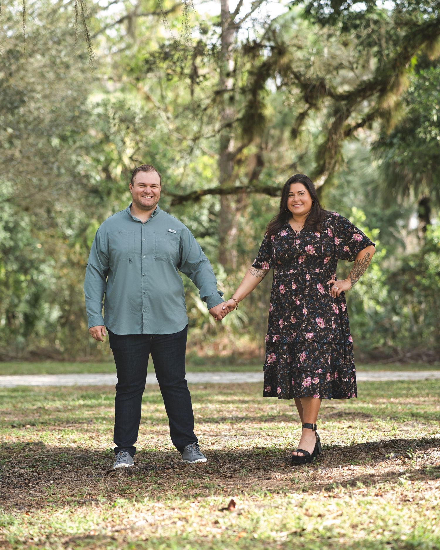 Couple in casual attire holding hands while walking through a scenic park.