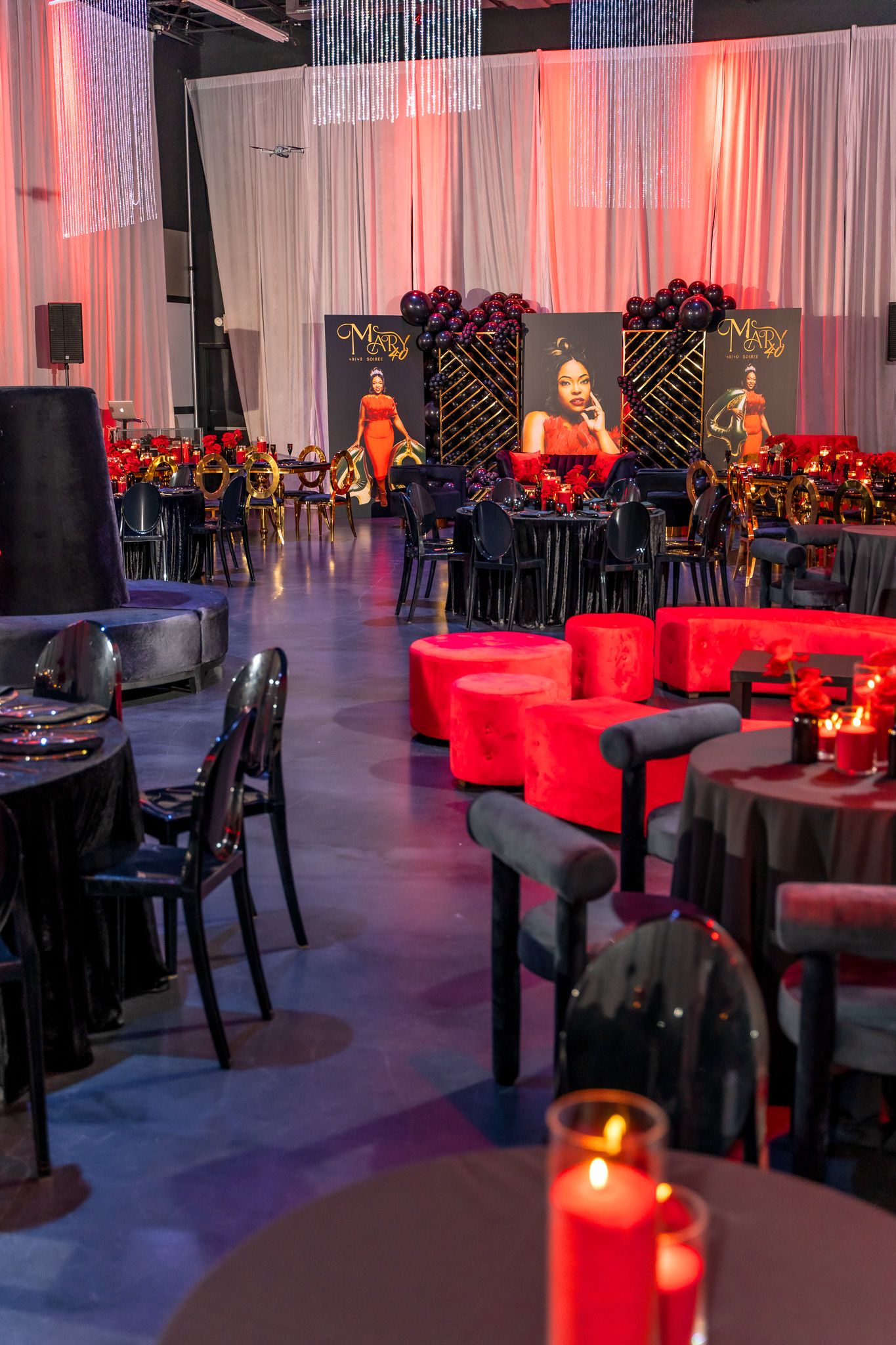 Elegant party venue with red and black decor, featuring white curtains and mood lighting.