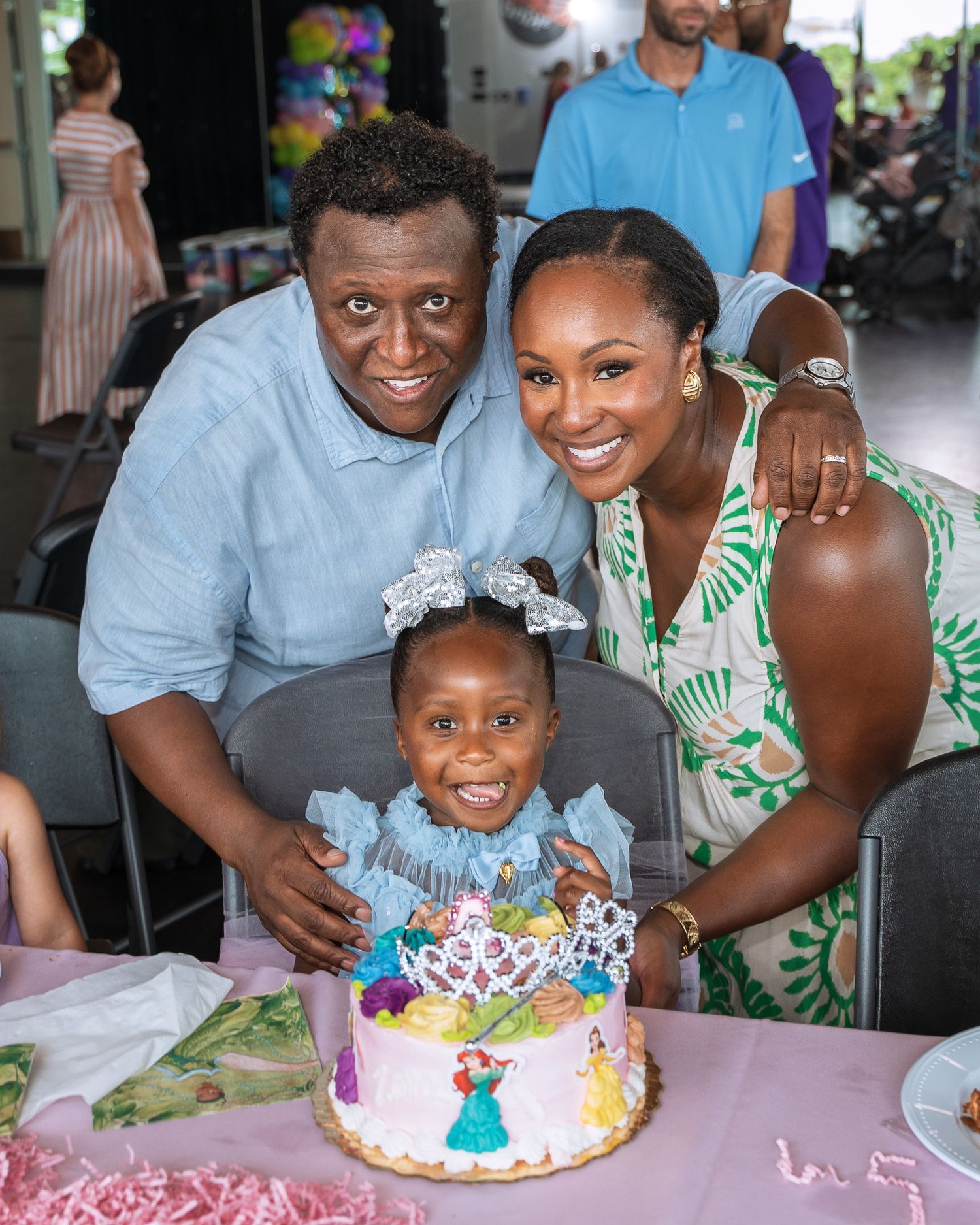 A family celebrates together around a pink birthday cake at a festive party.