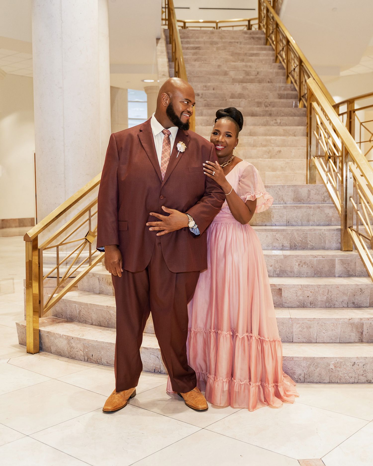 A couple poses together on marble stairs, showcasing their coordinated formal attire.