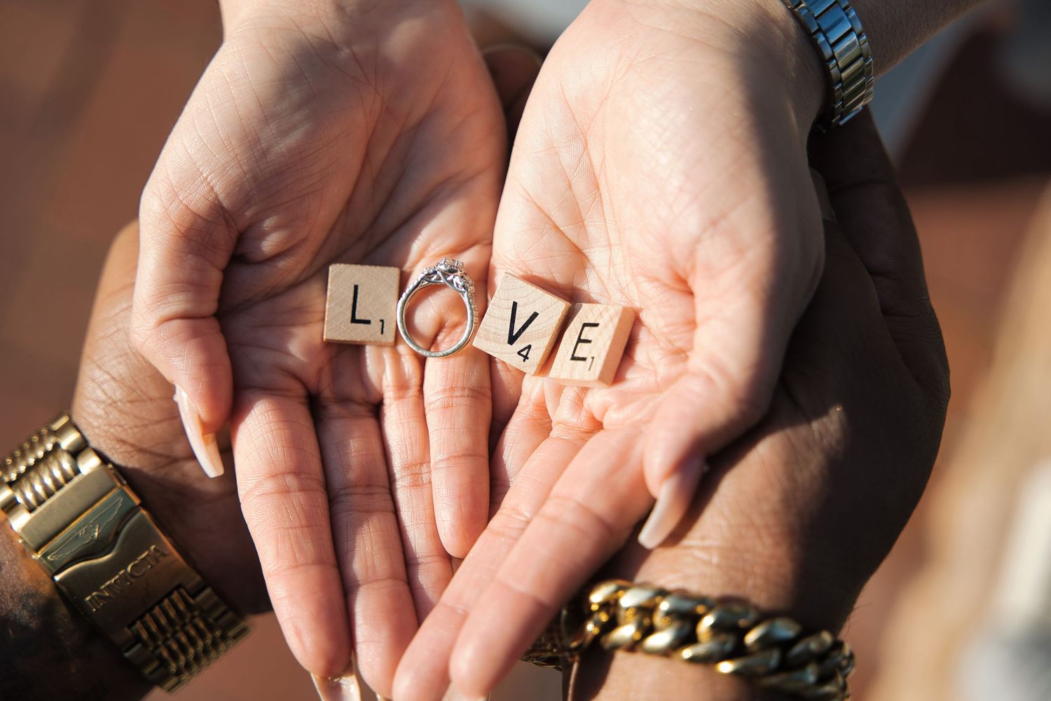 Hands holding wooden letter tiles spelling out LOVE against a dark background.
