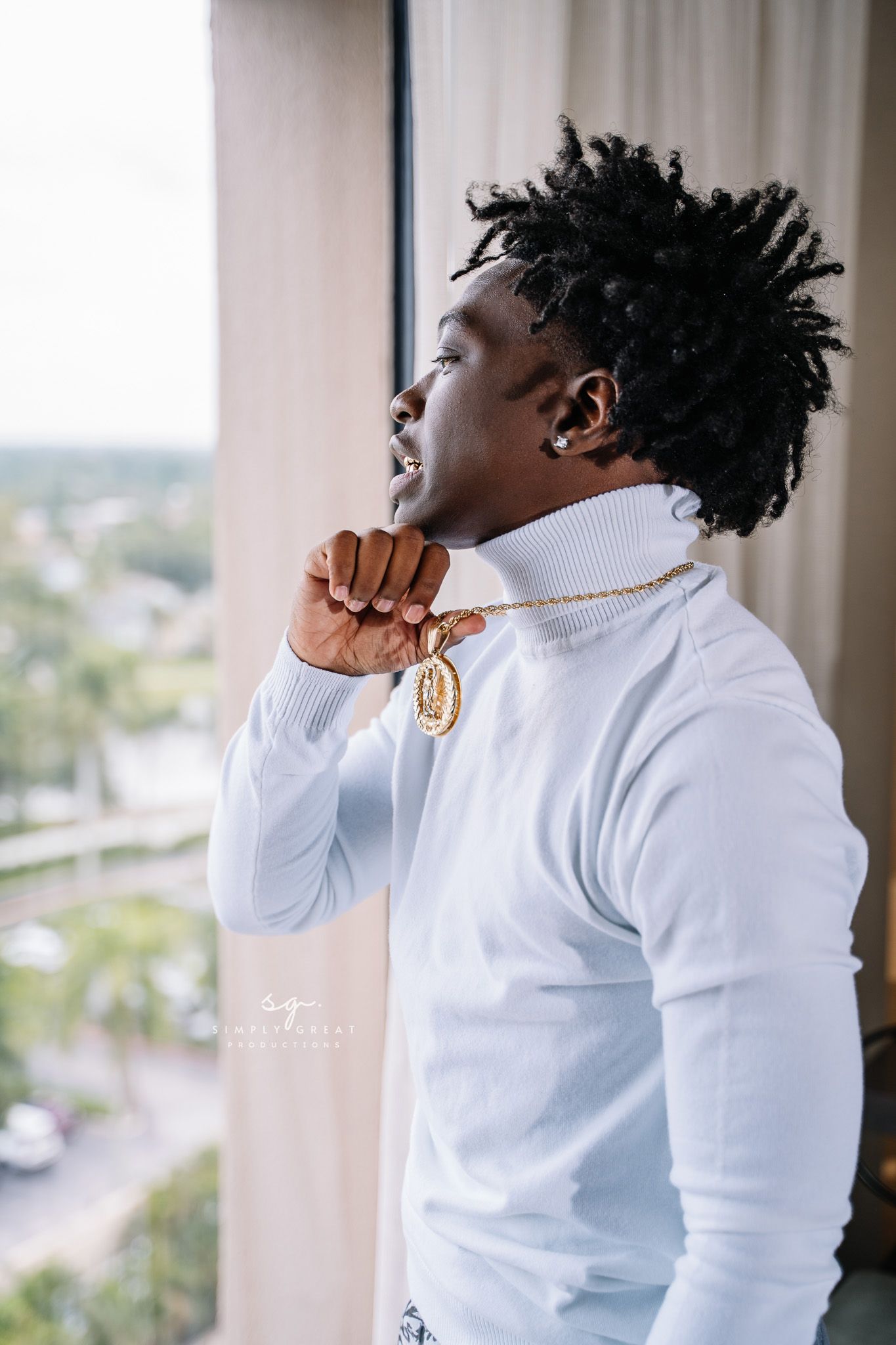 Person in white turtleneck sweater with gold necklace looking to the side near window.
