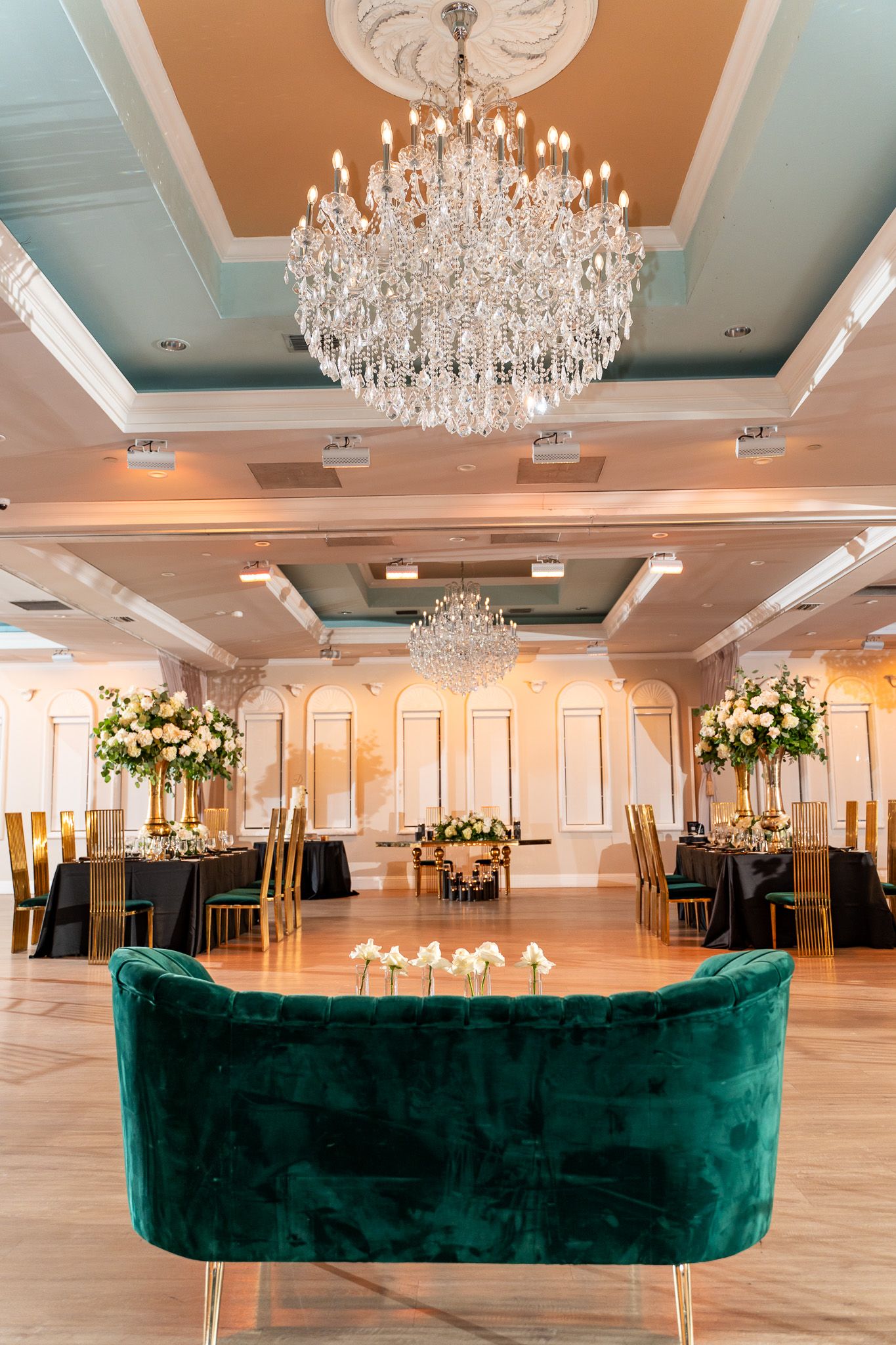 Luxurious ballroom with crystal chandeliers and emerald velvet seating for a wedding reception.