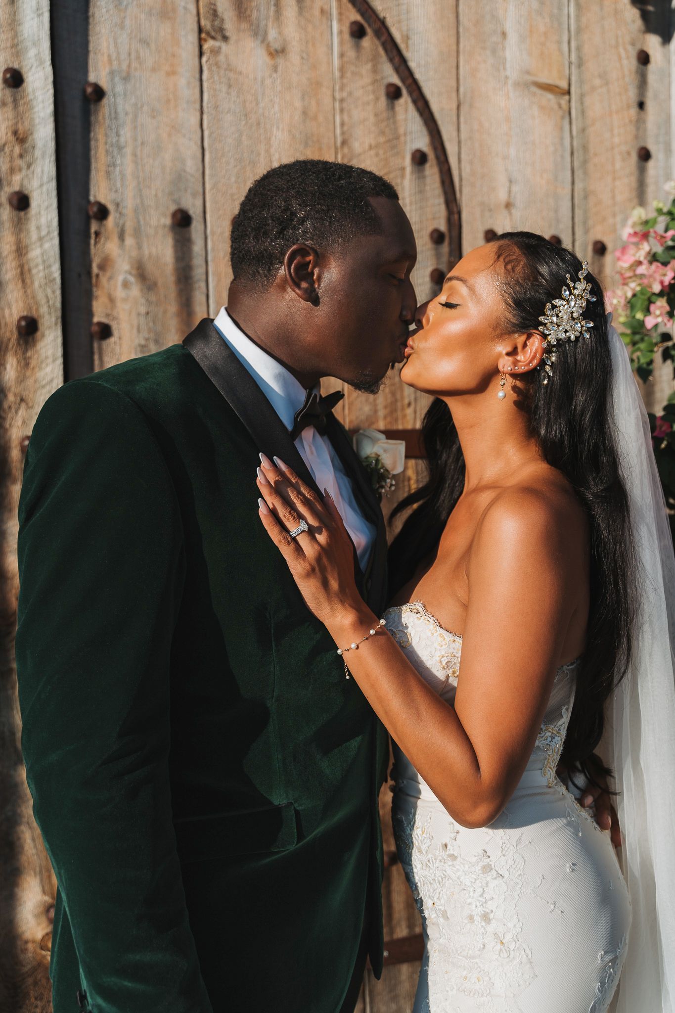 Romantic wedding portrait of couple sharing intimate moment against rustic wooden backdrop with pink flowers.