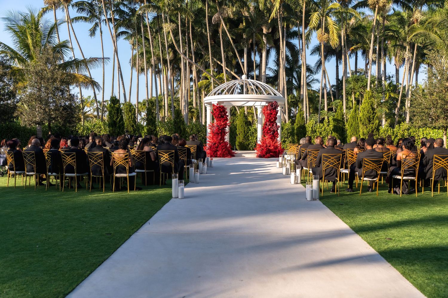 Palm trees line a white outdoor wedding aisle runner in a tropical garden setting.