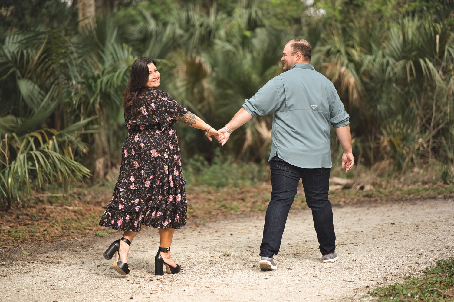 Couple holding hands while walking on a dirt path surrounded by tropical foliage.