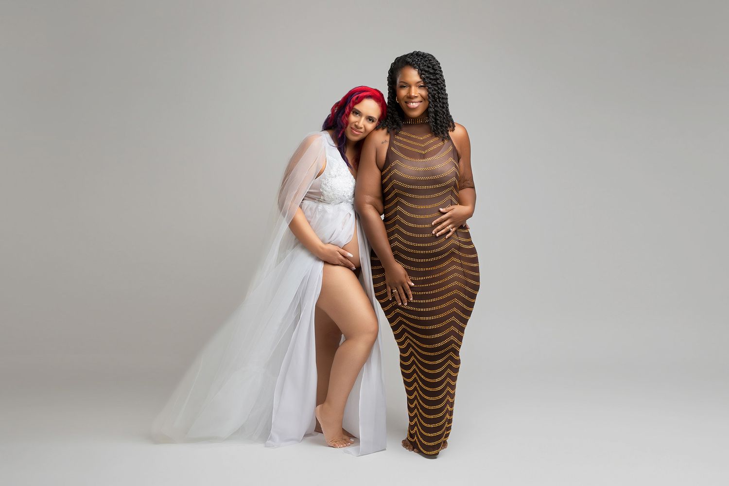 Two women posing together in contrasting dresses for maternity shoot.