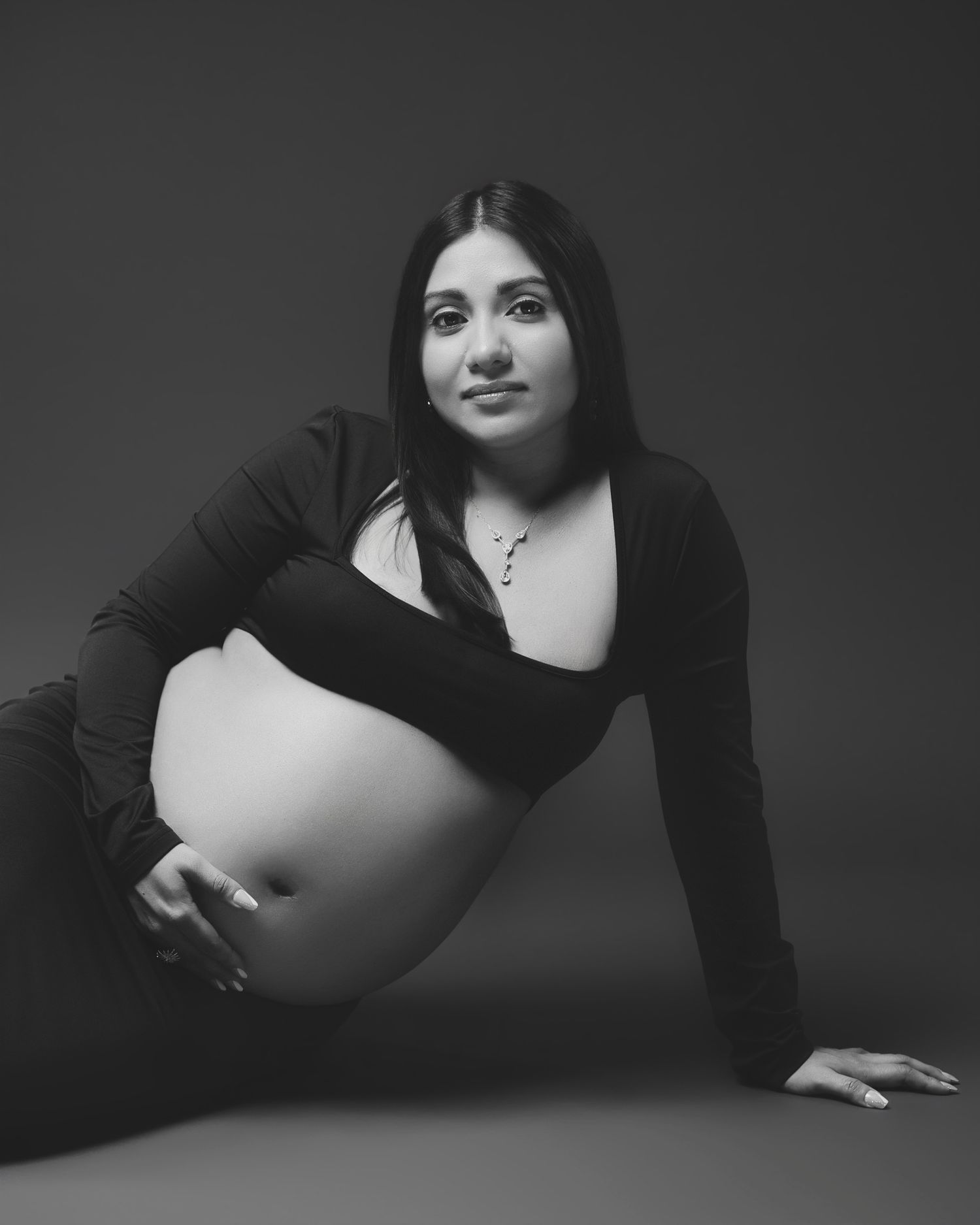 Black and white maternity portrait with figure in fitted black attire against dark background.