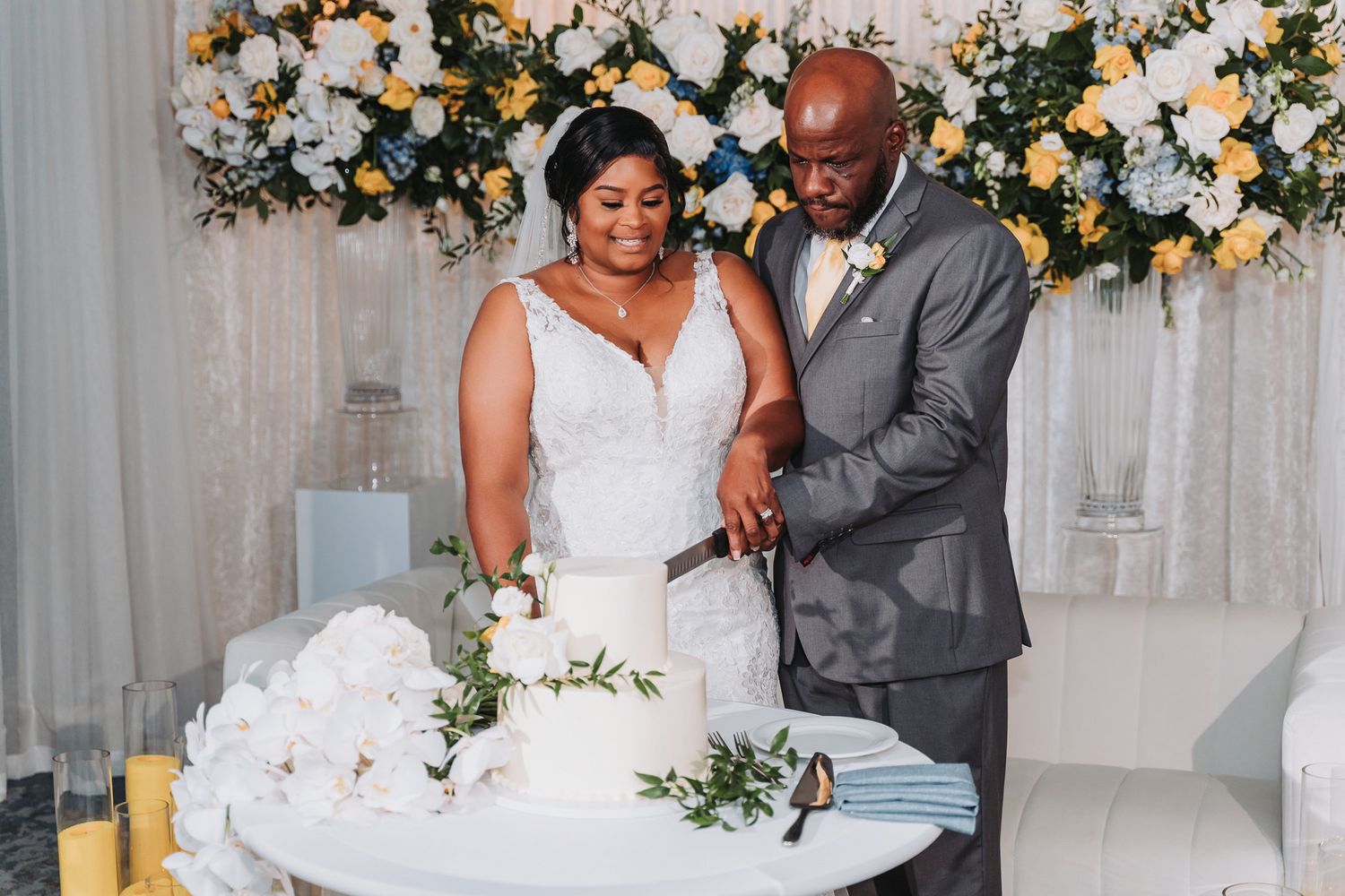 Newlywed couple cutting their wedding cake decorated with white floral arrangements.