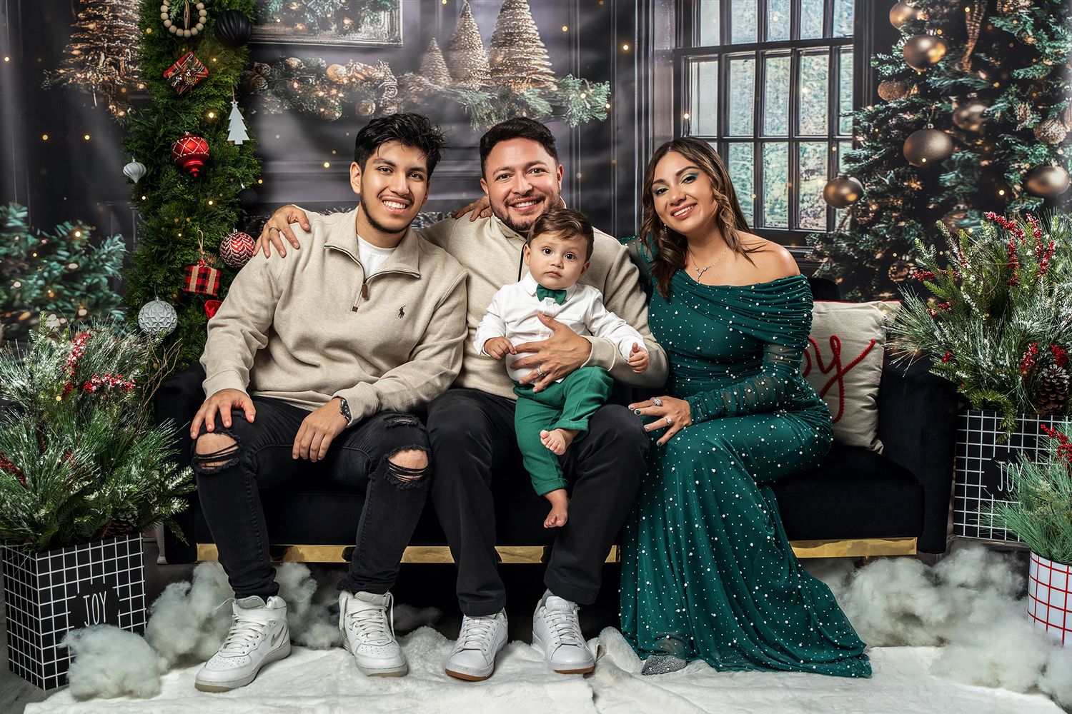 Family holiday portrait with Christmas tree and coordinated outfits in studio setting.