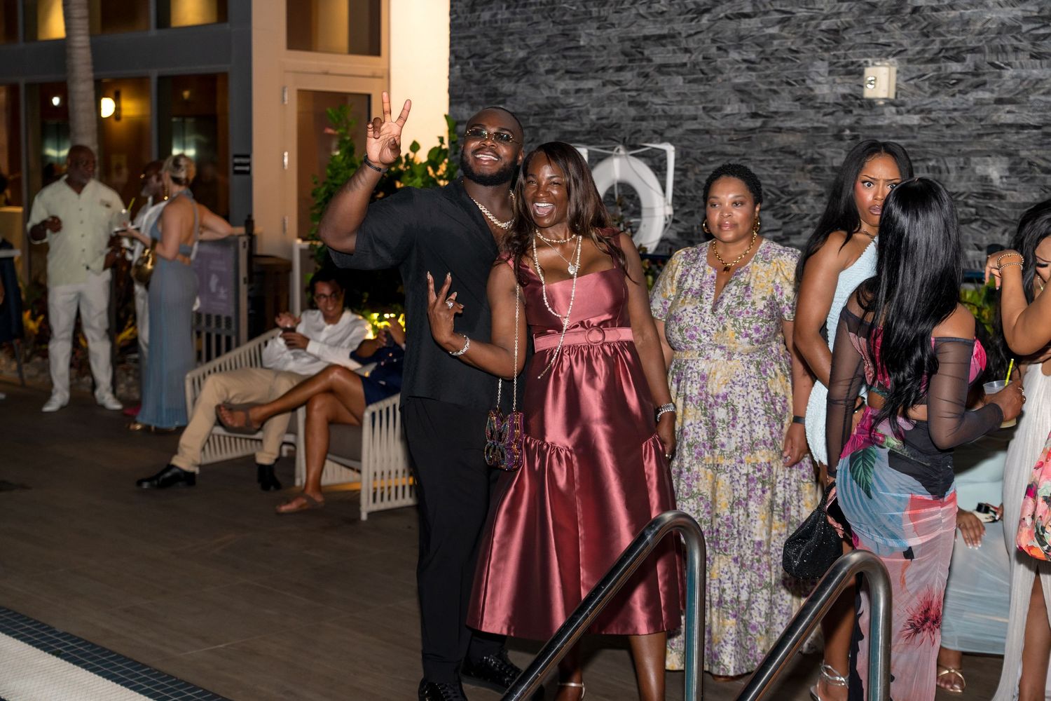 Group of guests socializing at an evening event with stone wall backdrop.