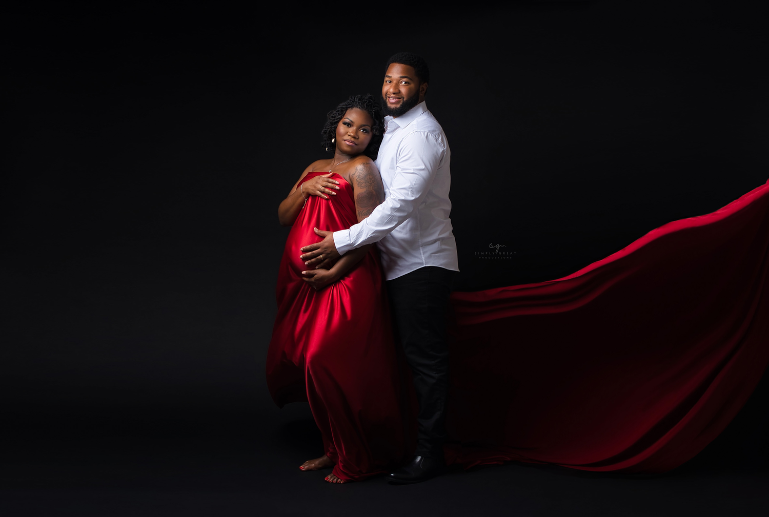 Dramatic maternity photo featuring a flowing red dress and intimate pose against a dark background.