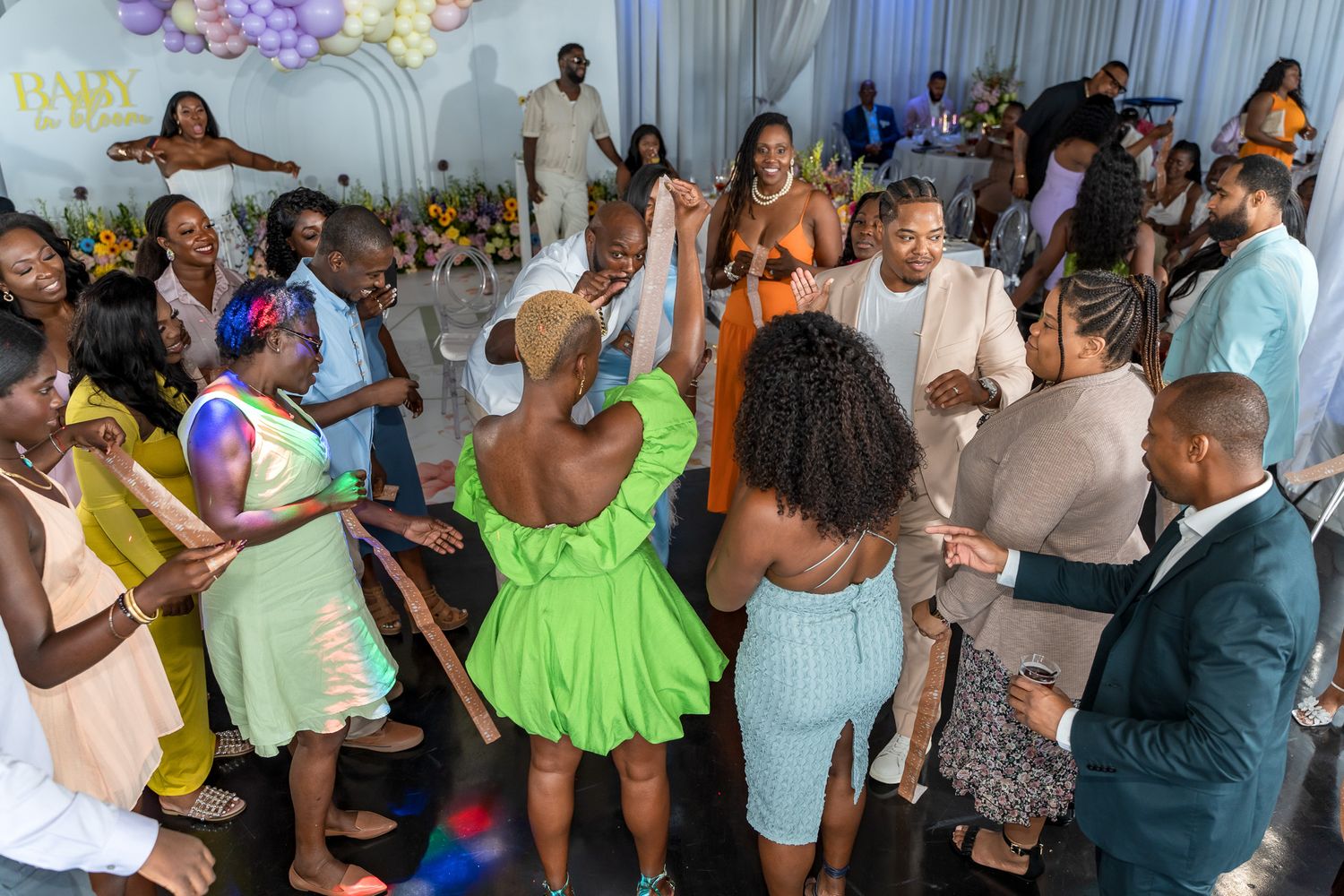 Lively dance party with guests in colorful attire under decorative balloon arrangements.
