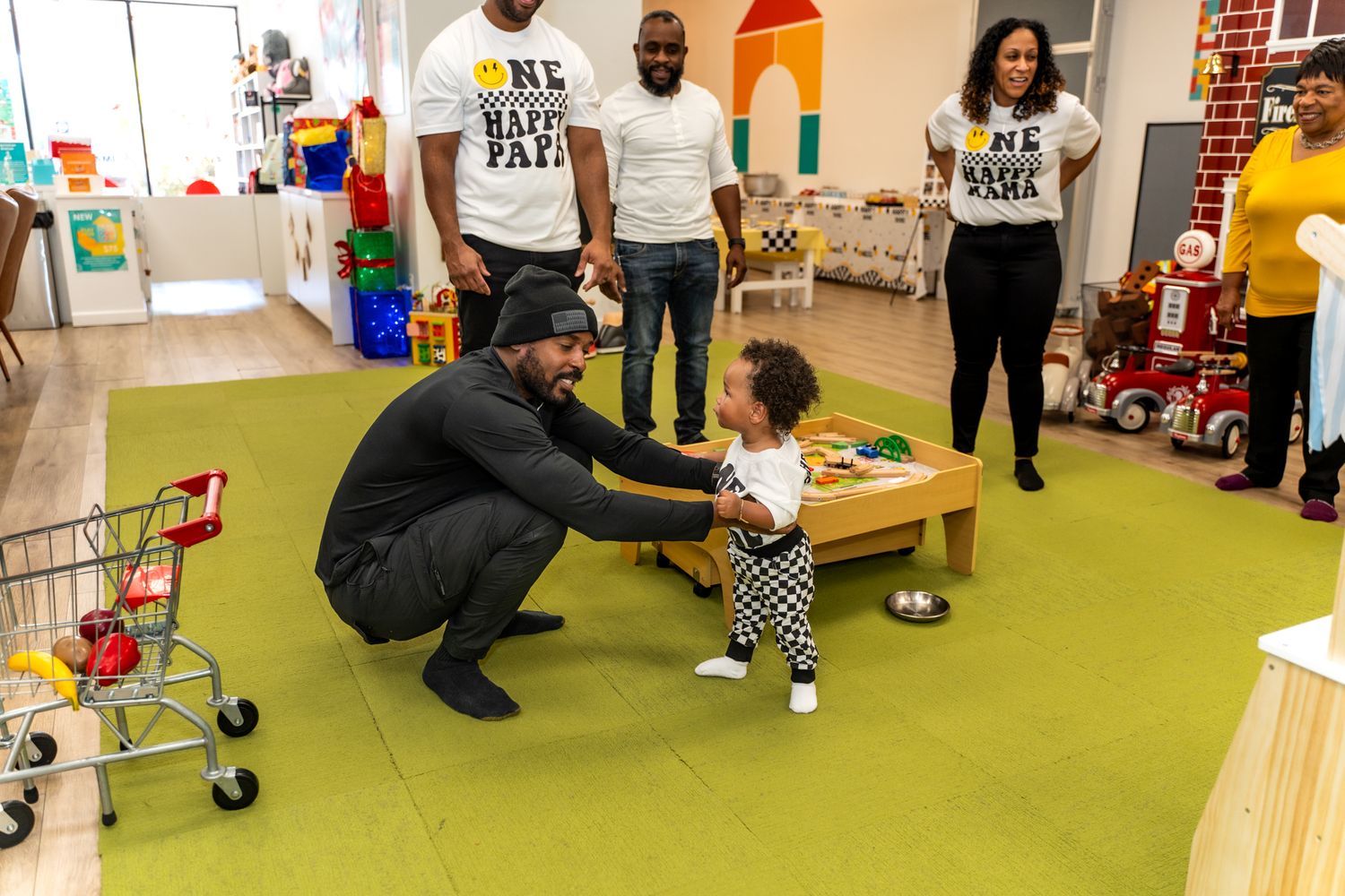 Adult kneeling down to interact with toddler at play table in colorful playroom.