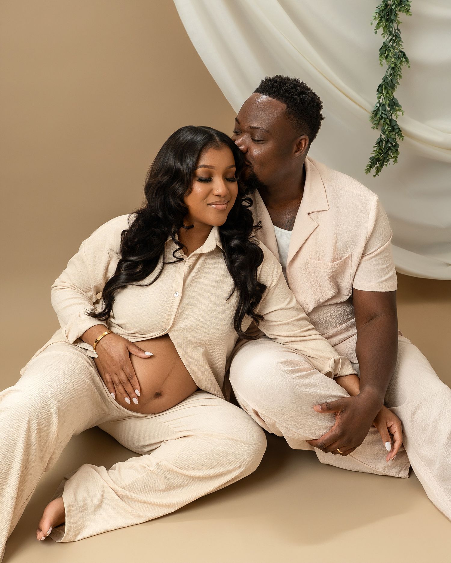 Intimate portrait of expecting couple in cream outfits sharing tender moment during photoshoot.