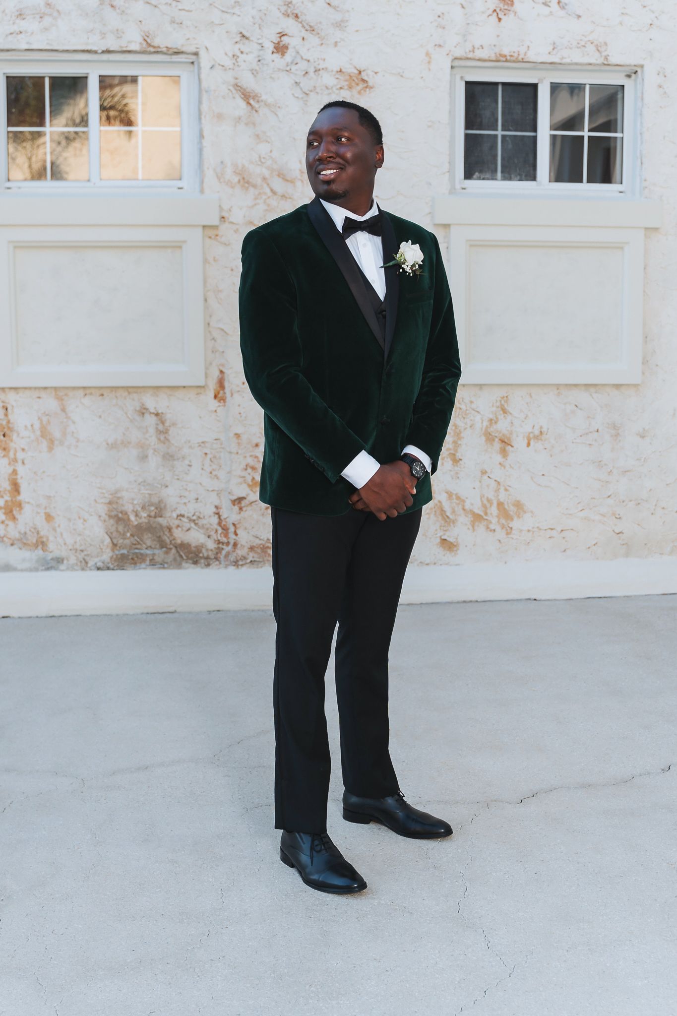 Groom poses confidently in emerald green velvet tuxedo jacket and black bow tie.