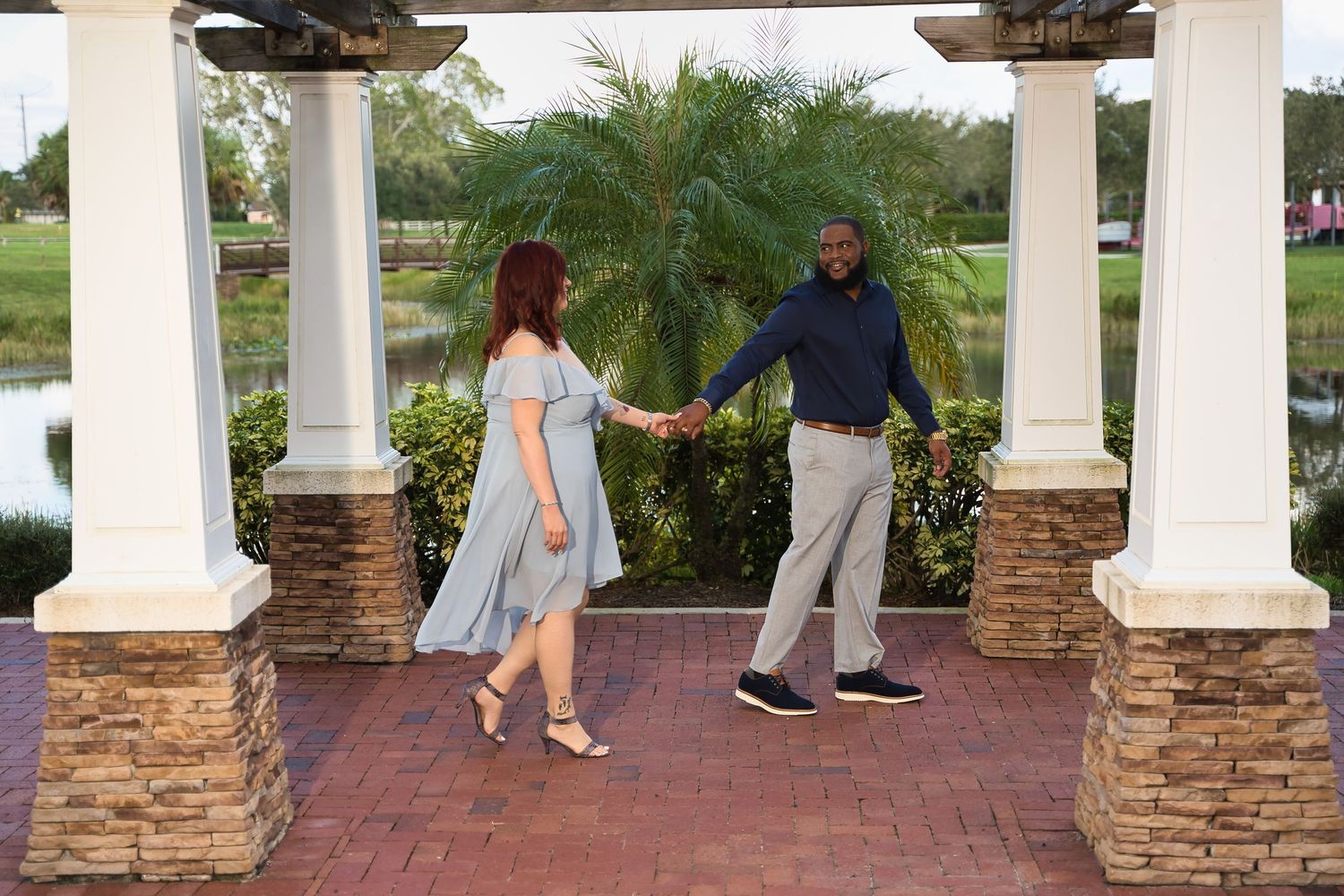 A couple dances together under a covered pavilion with stone pillars and tropical landscaping.