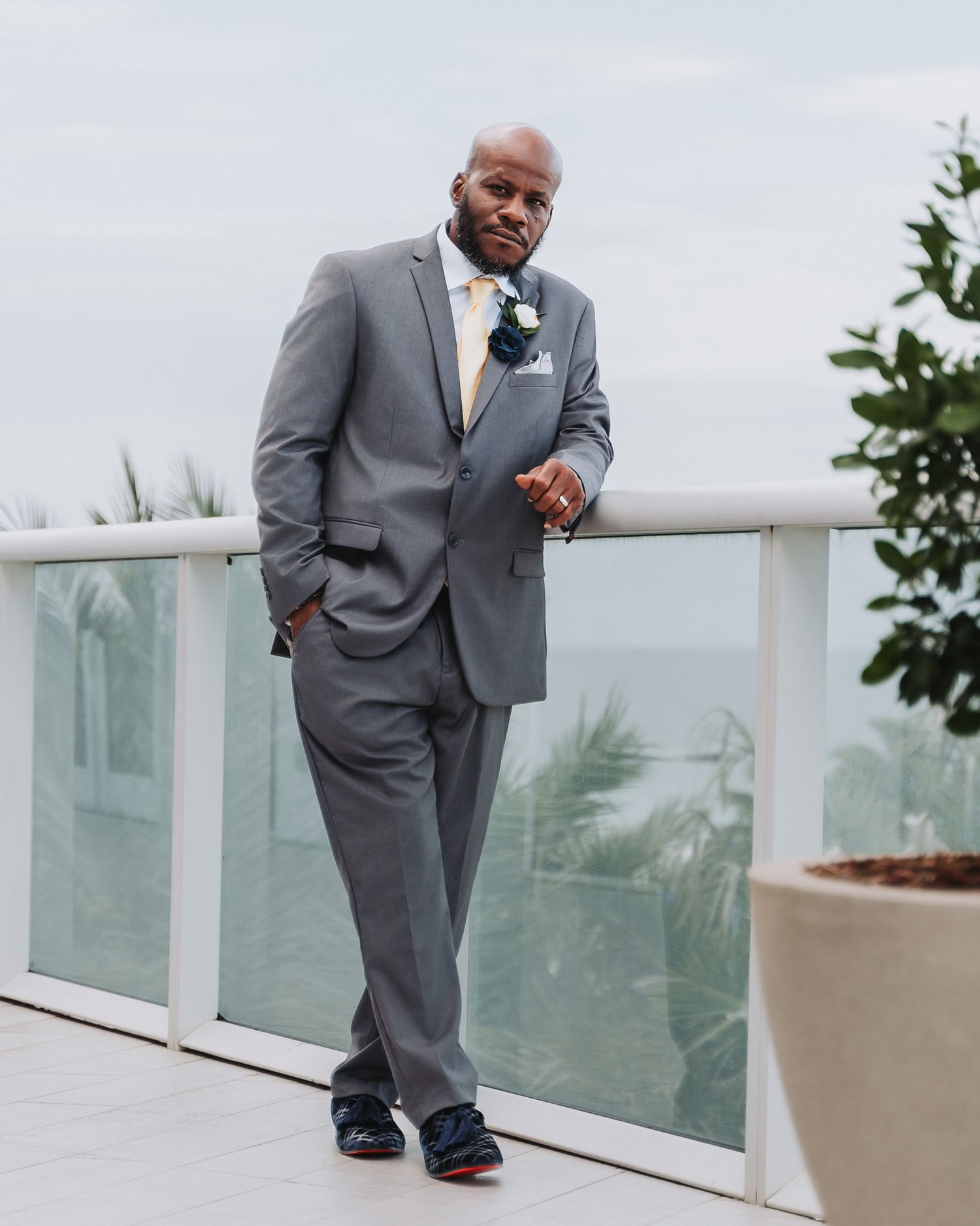 Groom in grey suit poses on outdoor balcony with cityscape background.