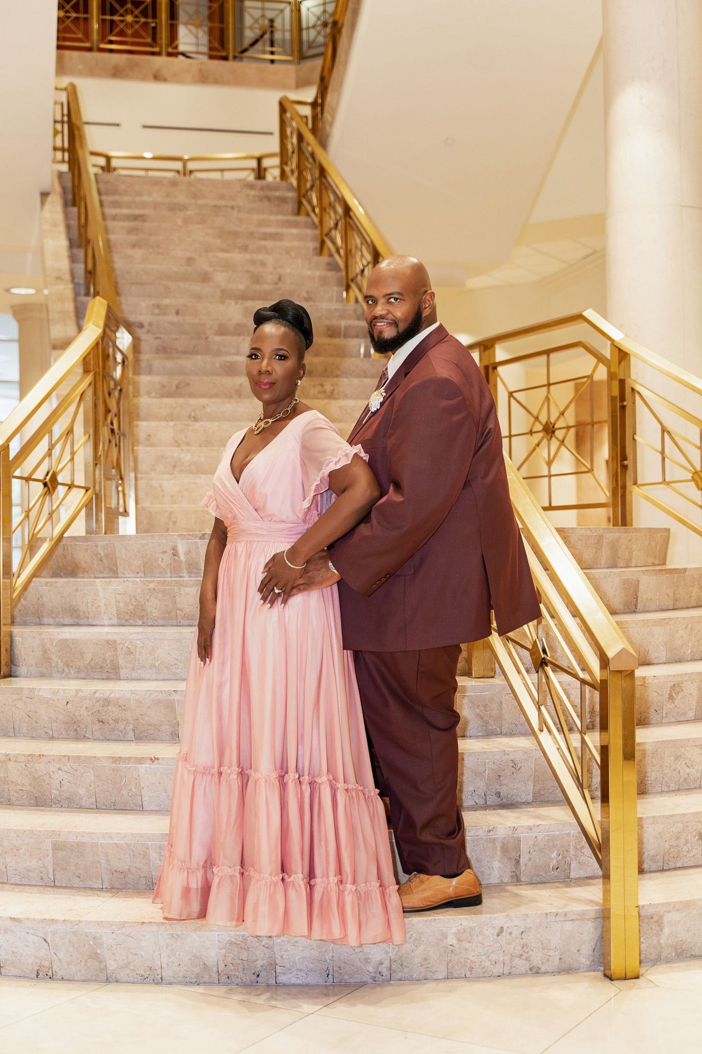 A couple poses confidently on marble stairs in coordinated formal wear.