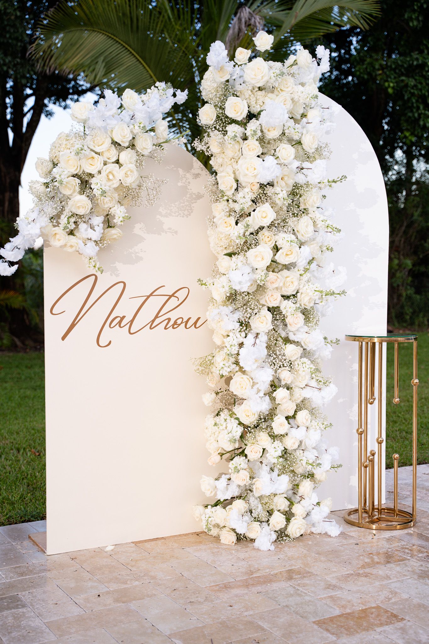 Elegant white curved backdrop with floral arrangements and gold script name 'Matthew' for wedding ceremony decor.