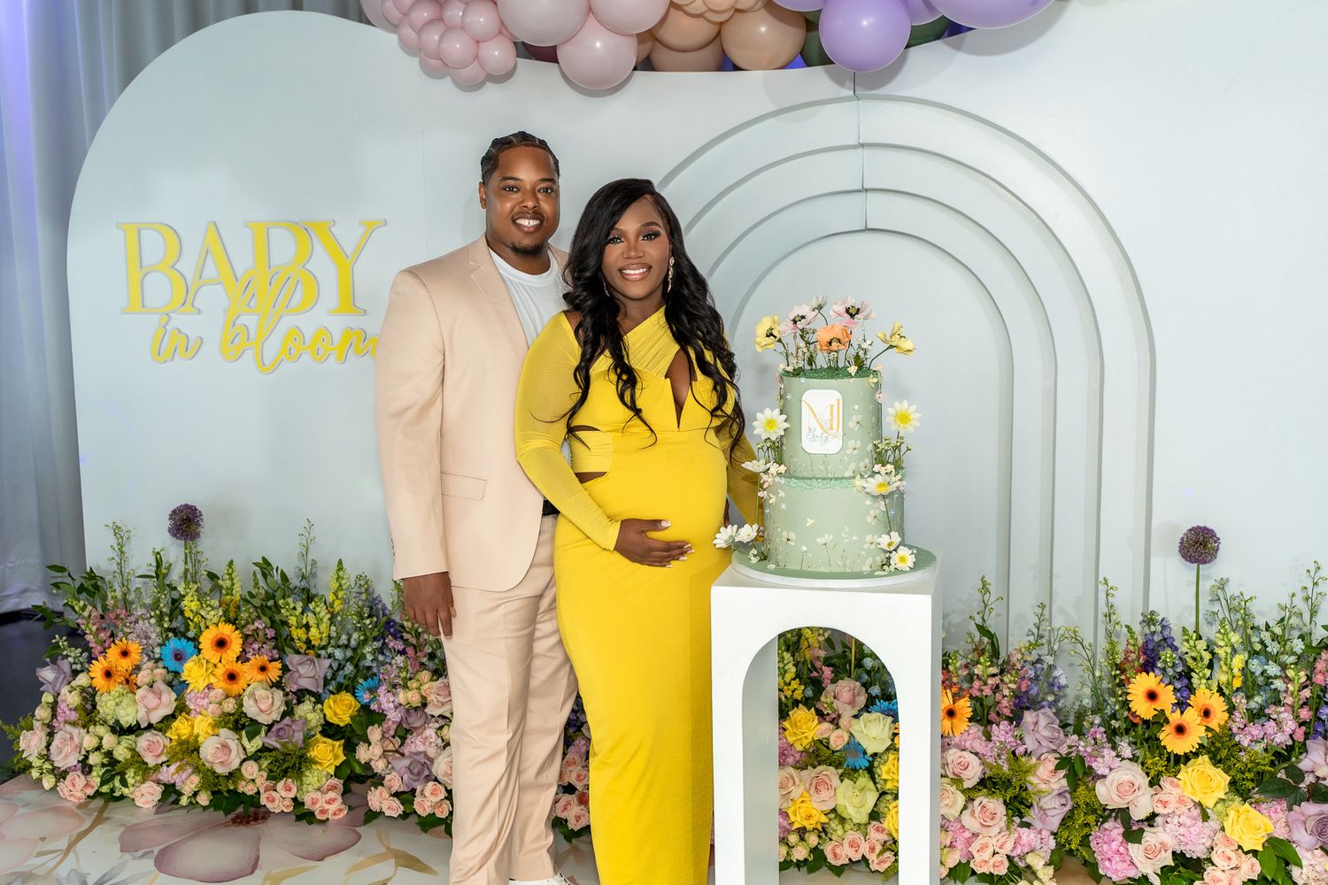 Baby shower celebration featuring a tiered cake and arched backdrop with floral decorations.