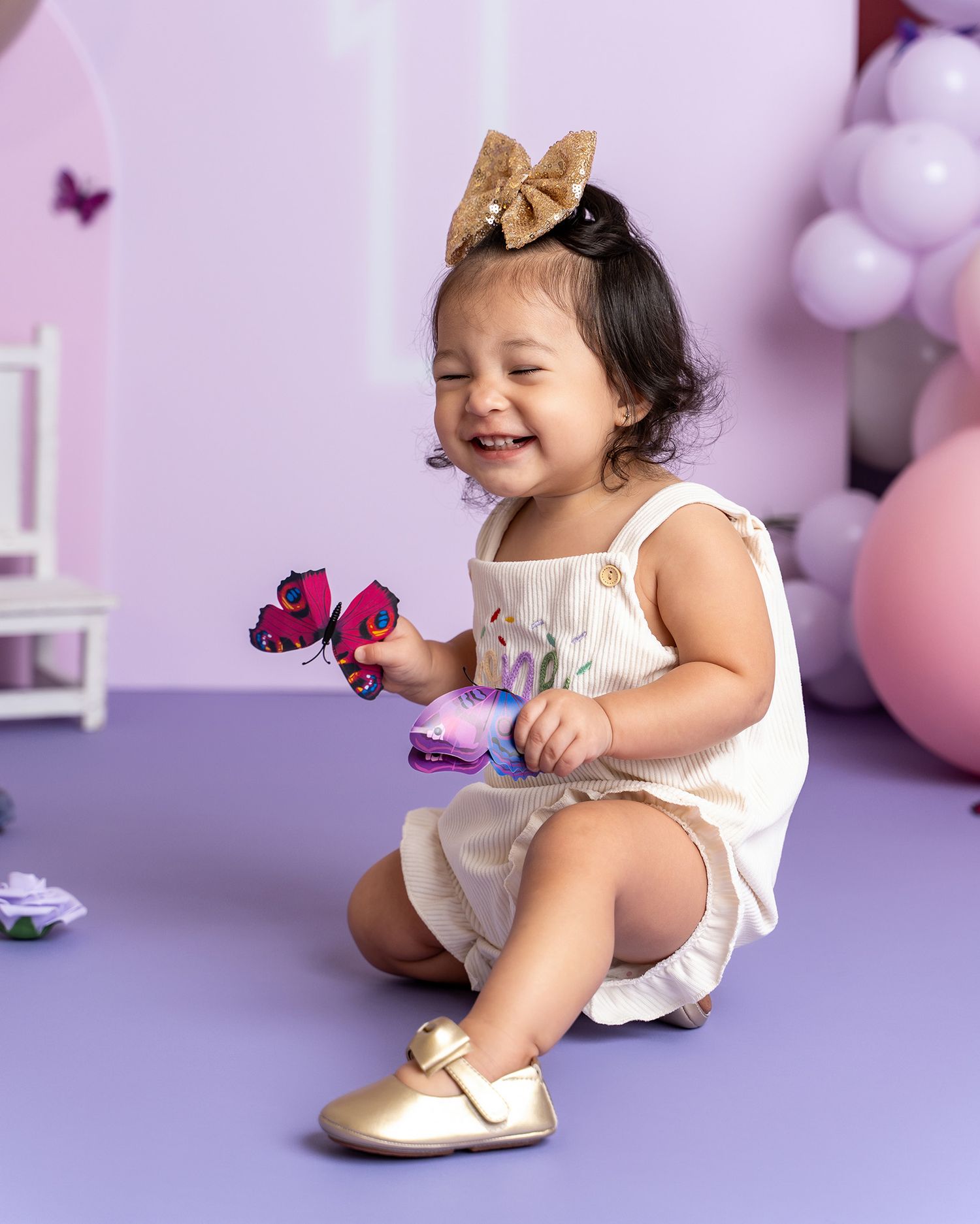A joyful child wearing a gold bow accessory plays with butterfly decorations on a purple background.