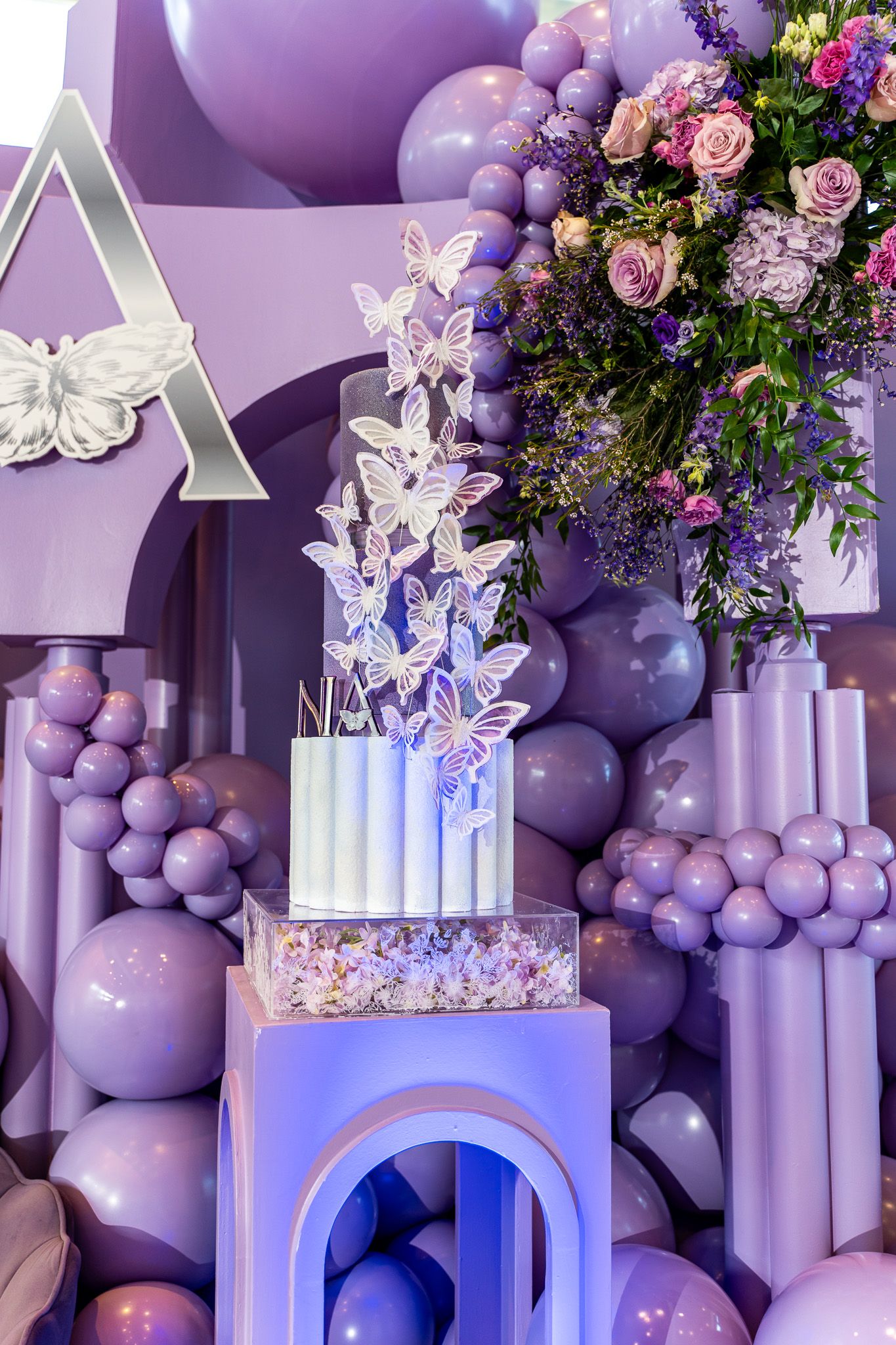 Stunning butterfly-themed cake display with purple balloon arch and floral arrangements.