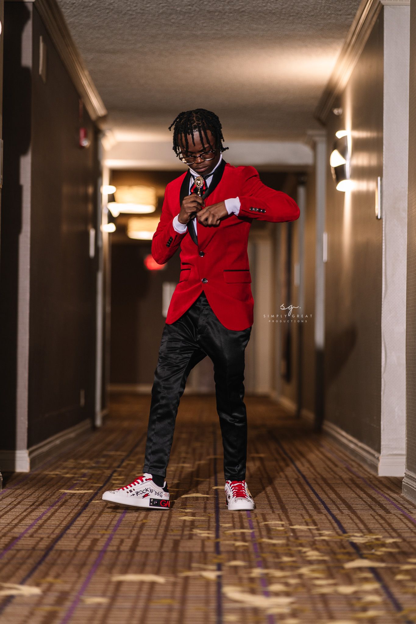 Stylish pose in red blazer and custom sneakers in hotel hallway.