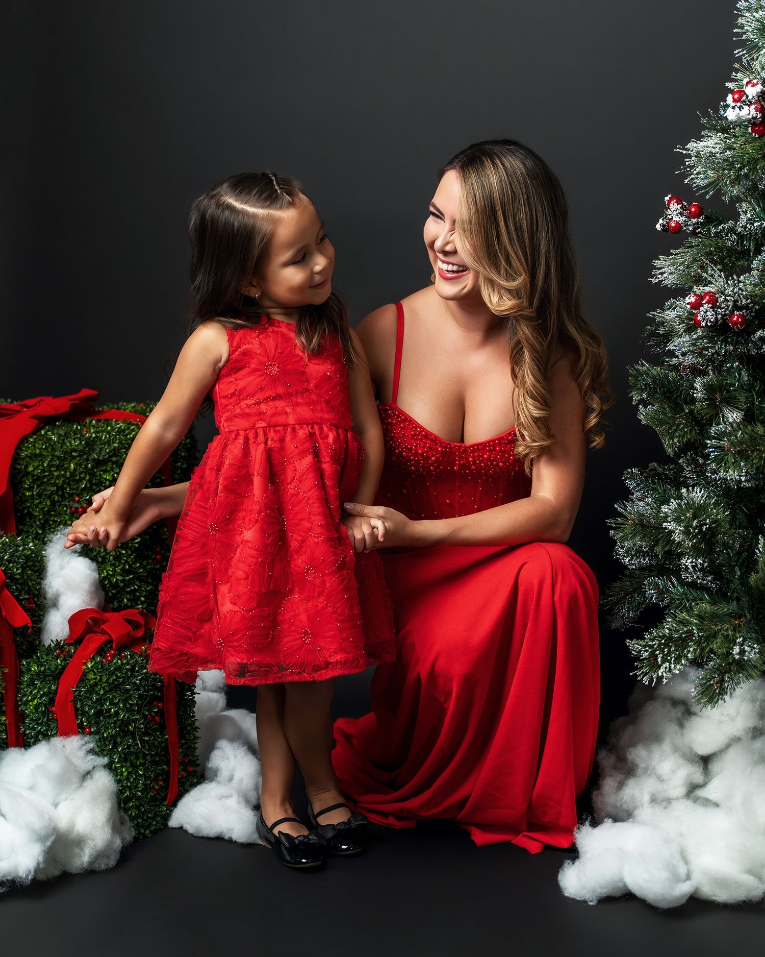 Two people in coordinated red holiday outfits share a joyful moment by a decorated Christmas tree.