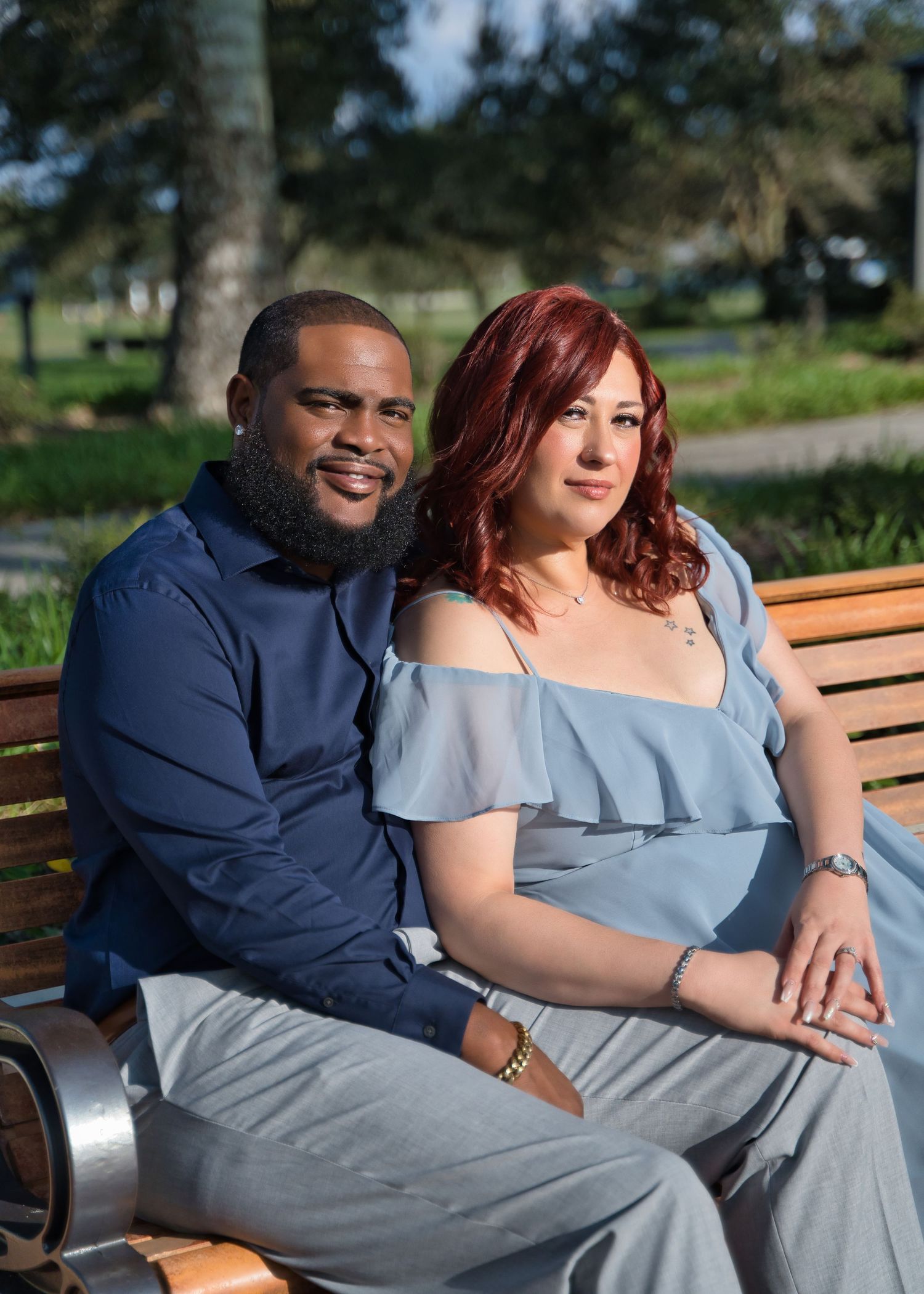 A couple sits close together on a park bench during an outdoor portrait session.