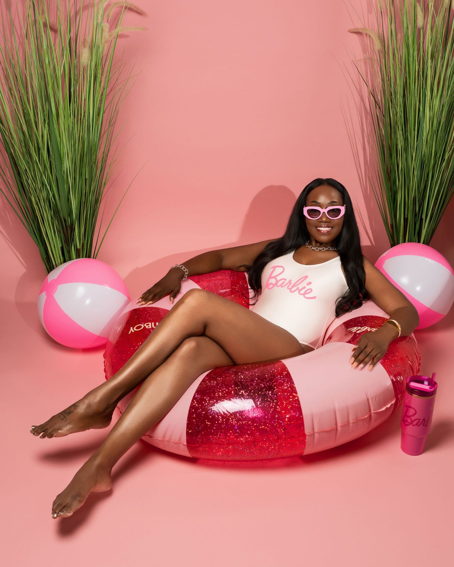 Luxurious summer scene with inflatable pink and clear pool float against pink backdrop with decorative grass plants.