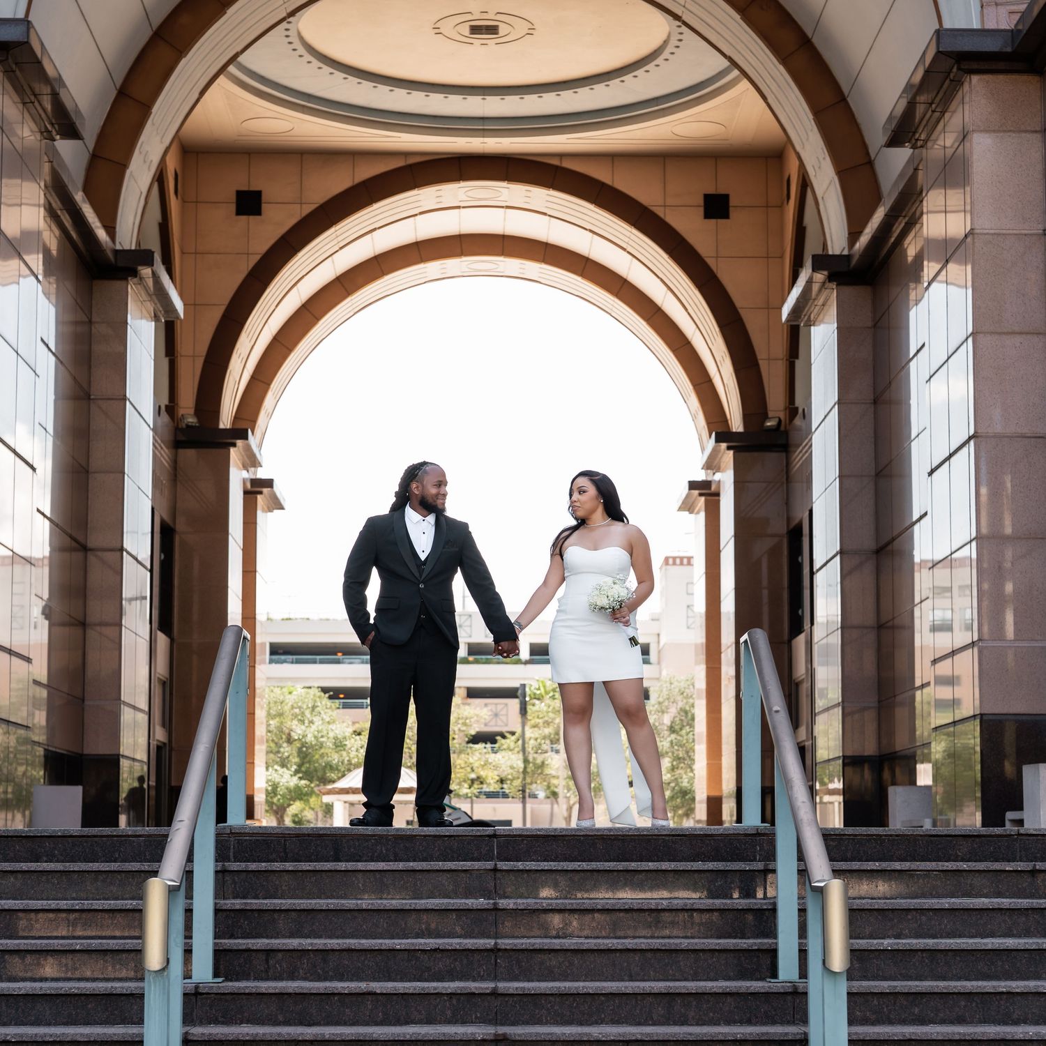 Bride and groom stand along a colonnade walkway with arched architecture and pillars during their wedding photoshoot.