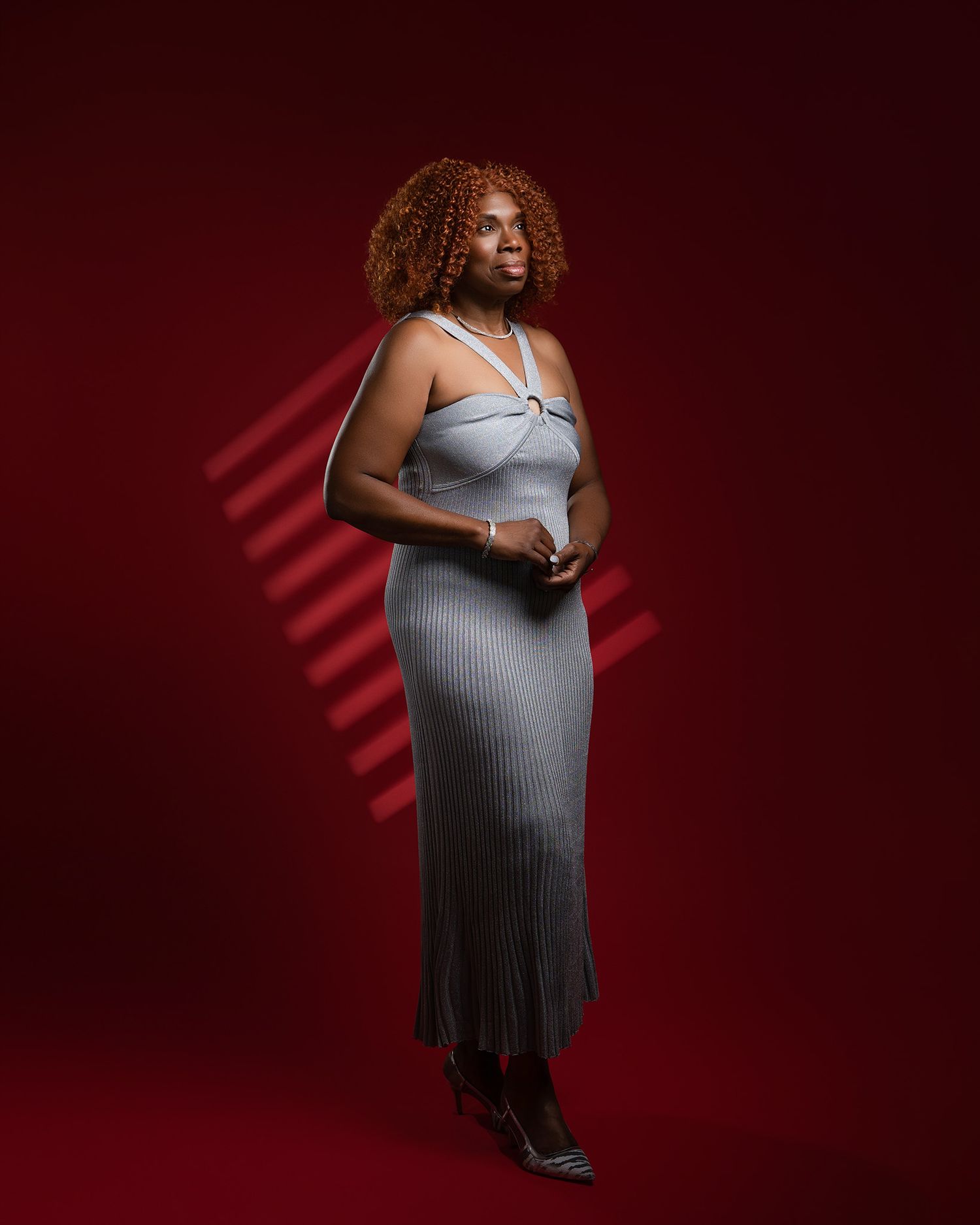 Full-length fashion portrait in grey dress against dramatic red background.