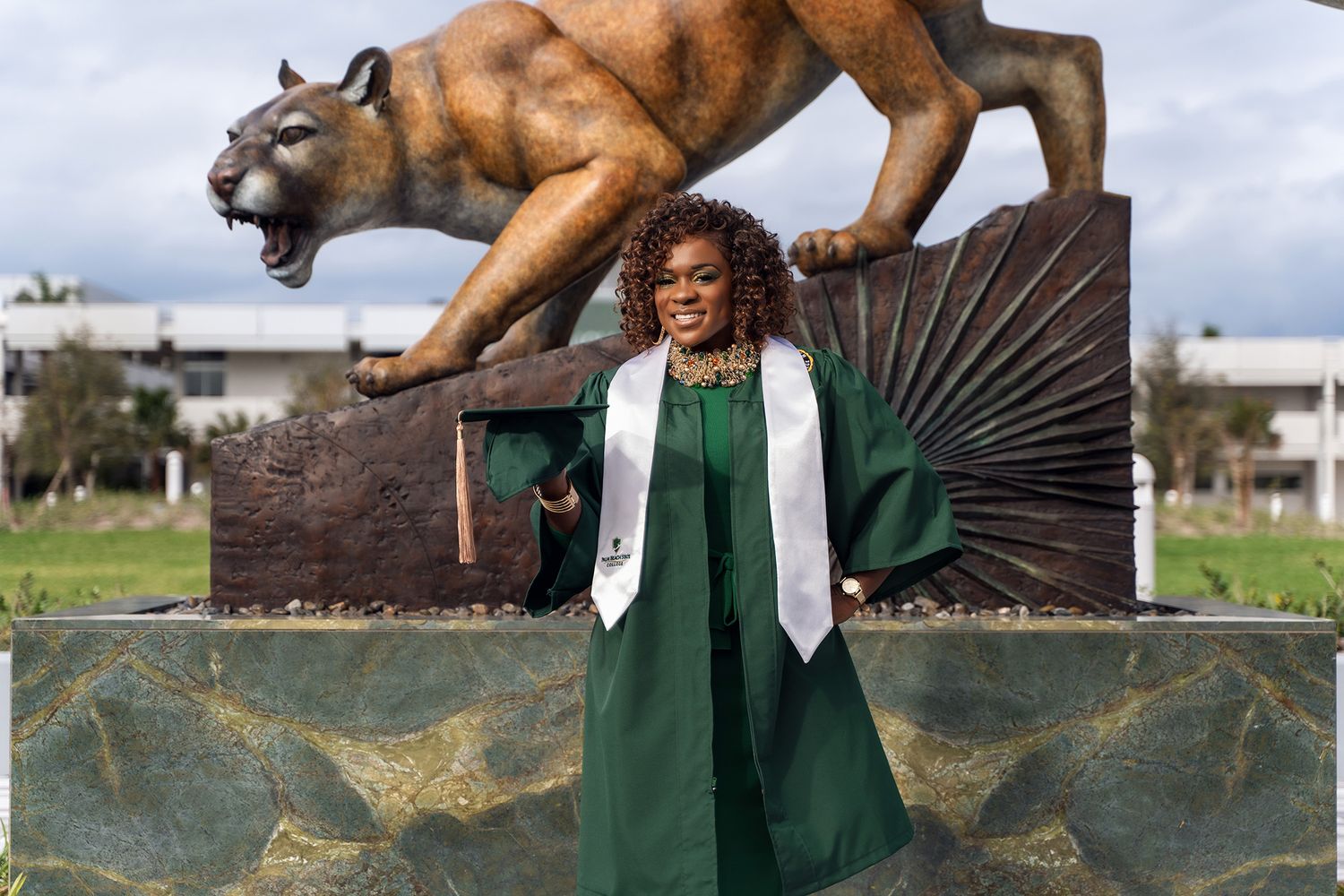 Graduate in academic regalia poses beneath bronze mountain lion monument.