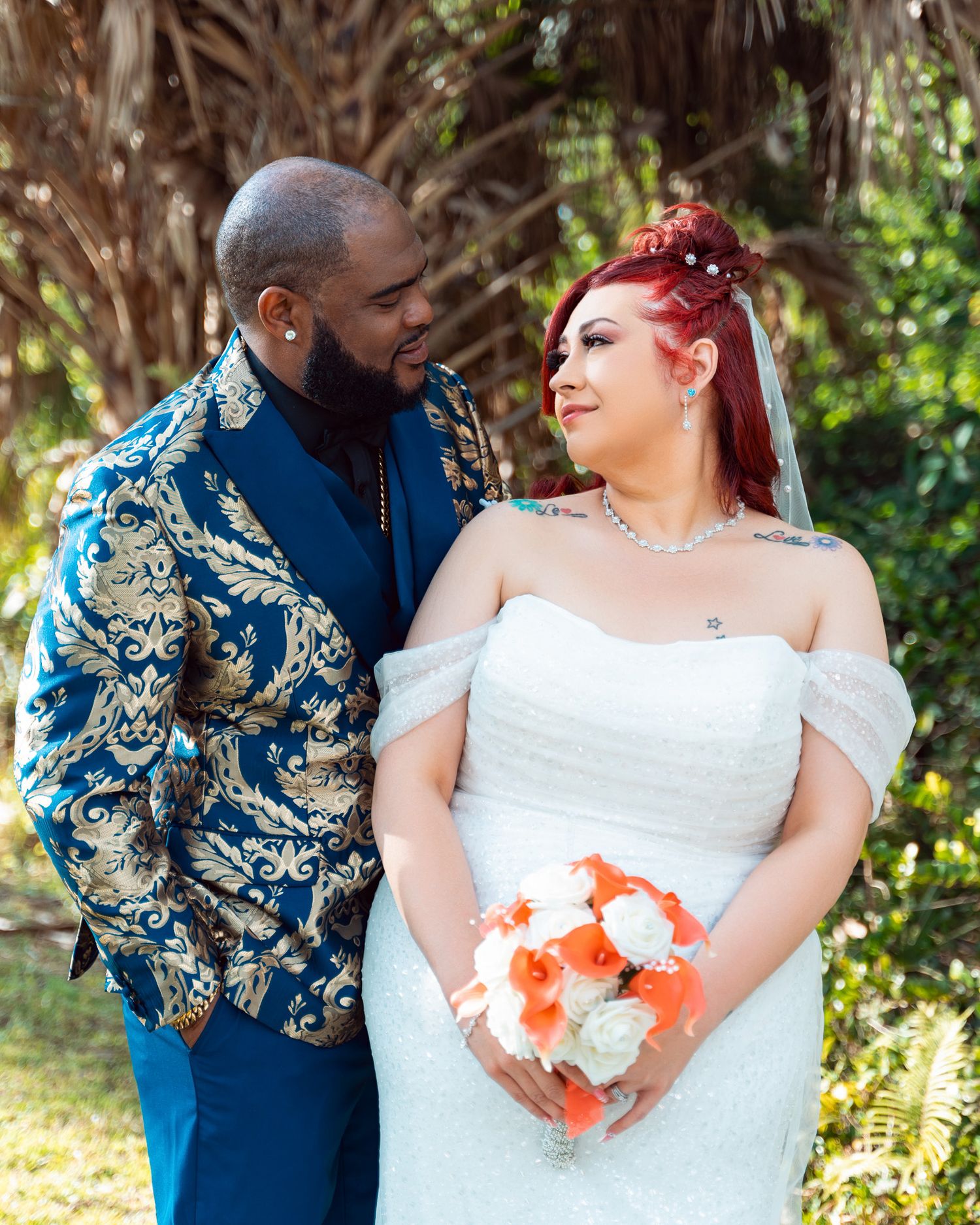 Newlyweds share a joyful moment outdoors with the bride holding orange and white flowers.