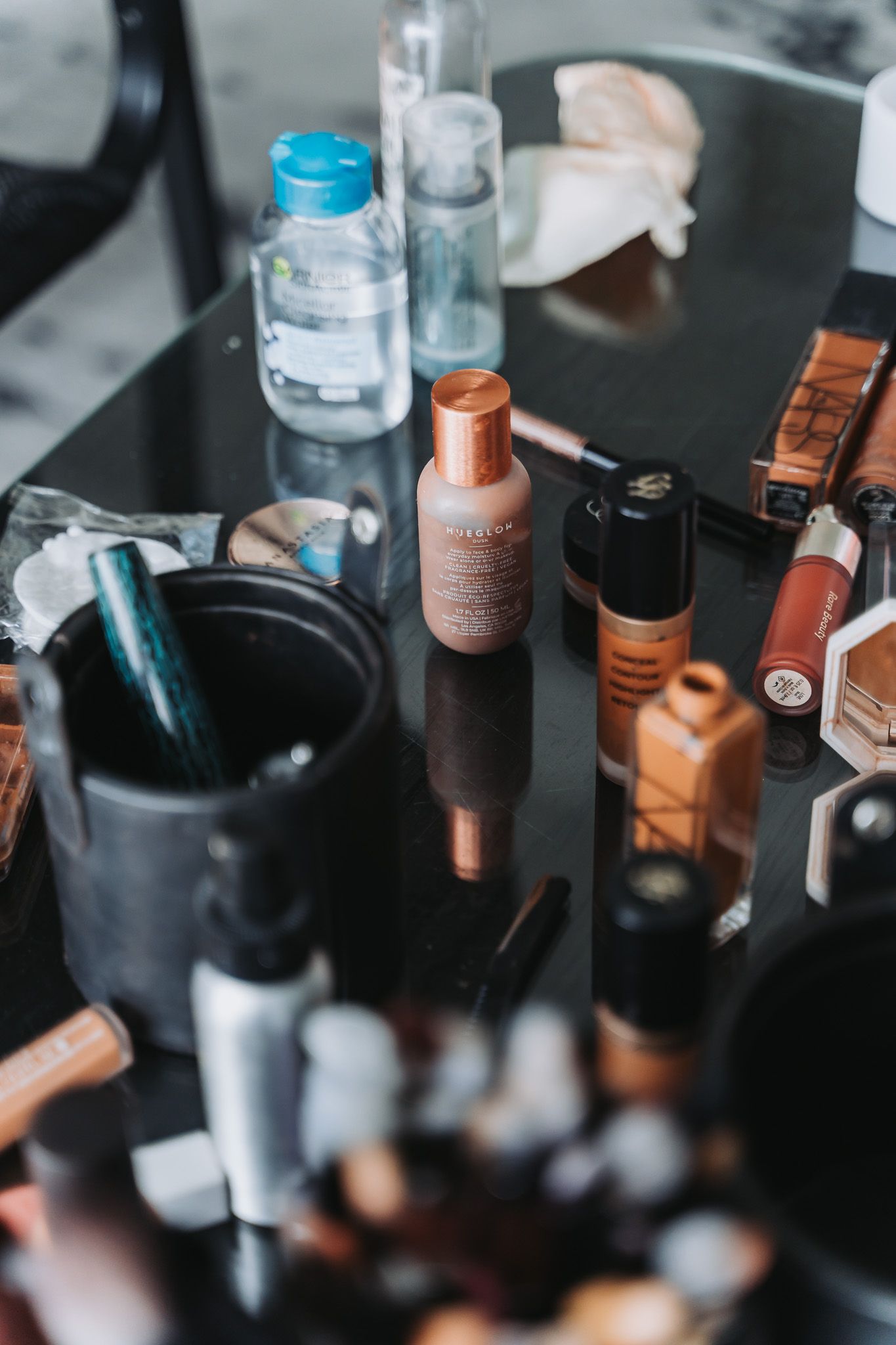Makeup and beauty products including foundation bottles and brushes arranged on a dark reflective surface.