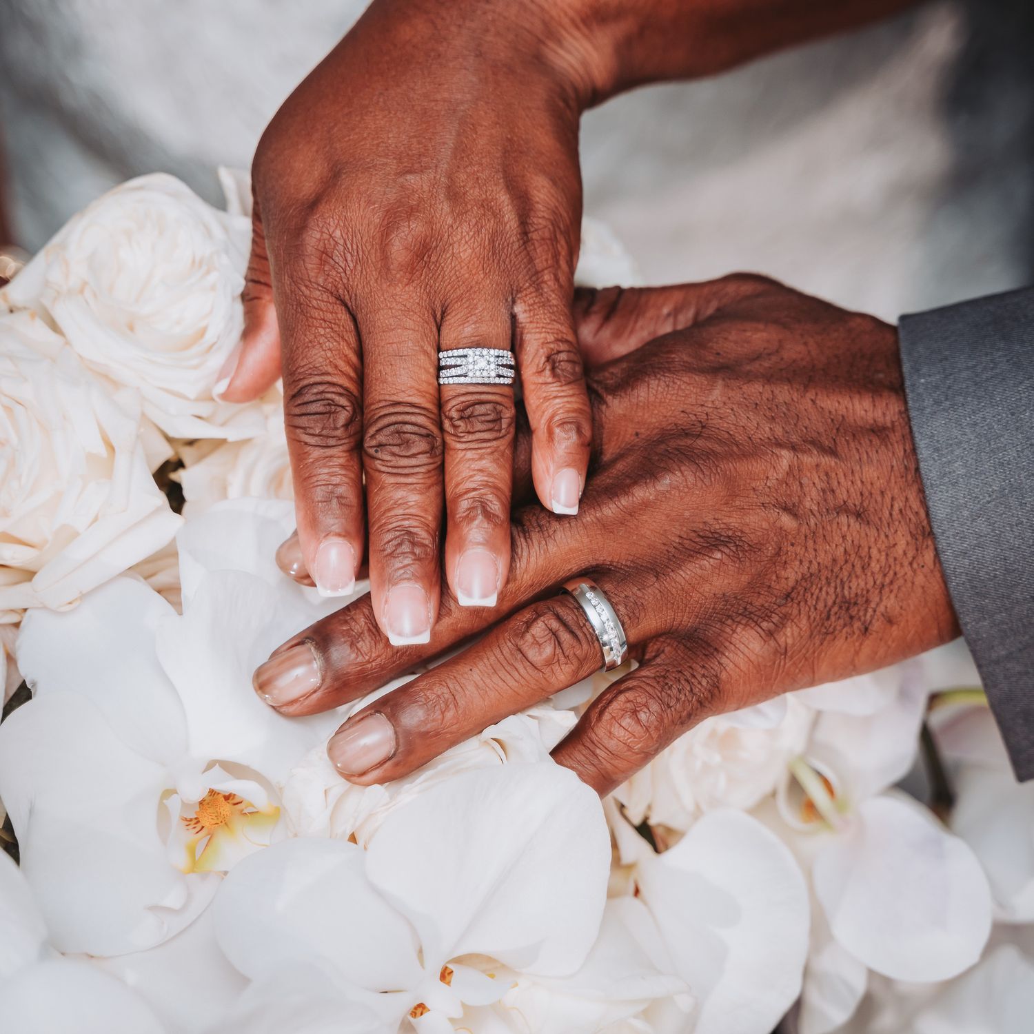 Close-up of wedding rings and hands resting on white orchid petals.