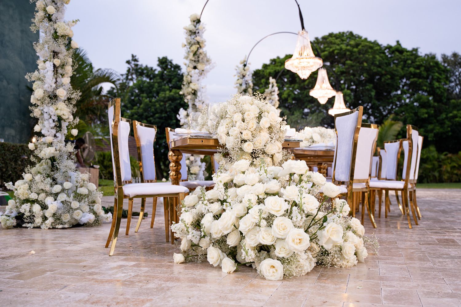 Romantic wedding ceremony setup with white floral arrangements and chairs on an outdoor patio near the ocean.