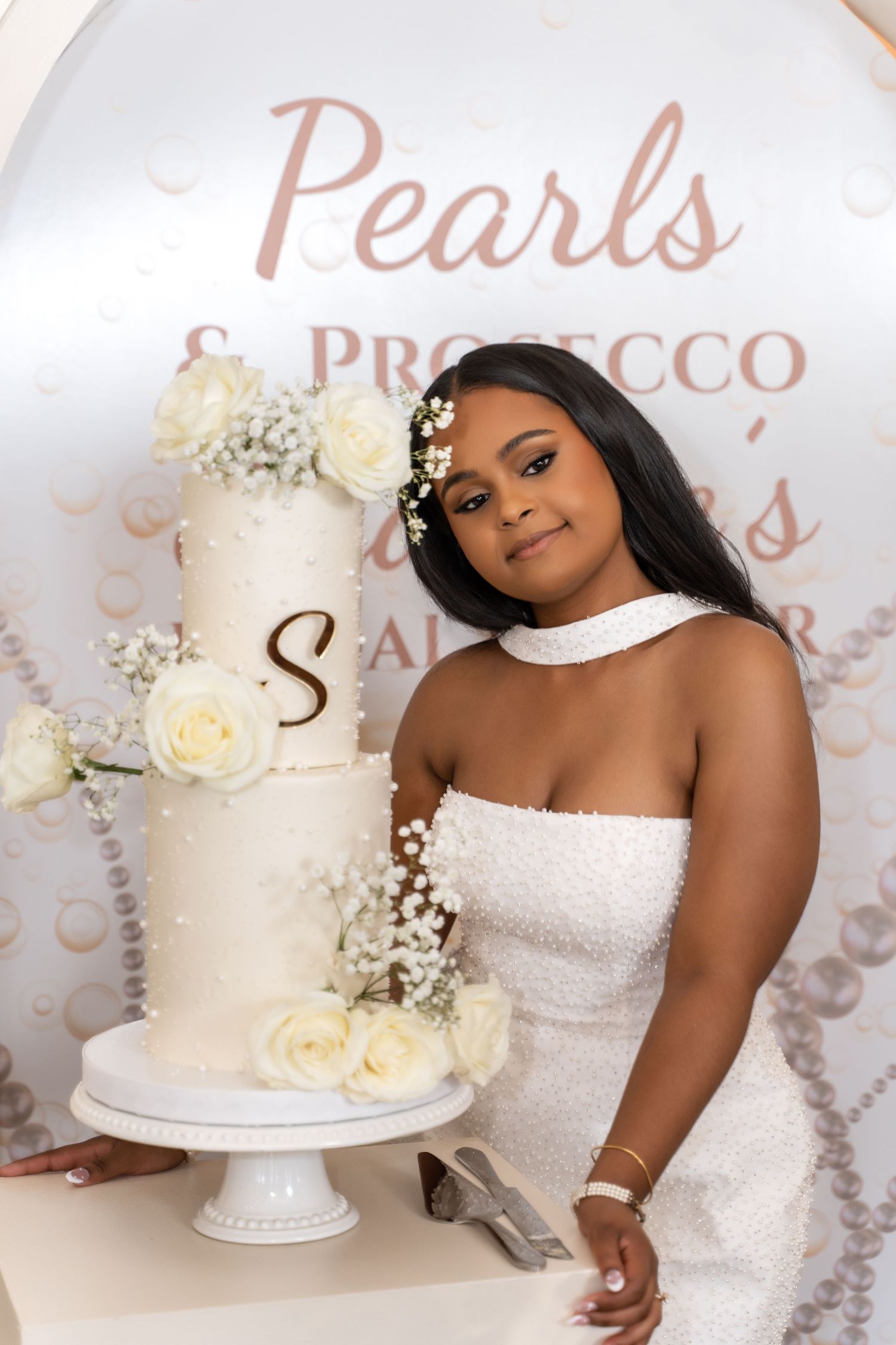 A stunning white wedding cake decorated with fresh white roses and pearls displayed on an elegant cake stand.