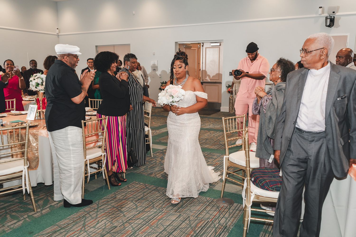 Wedding ceremony guests stand in an elegant venue with gold chiavari chairs.